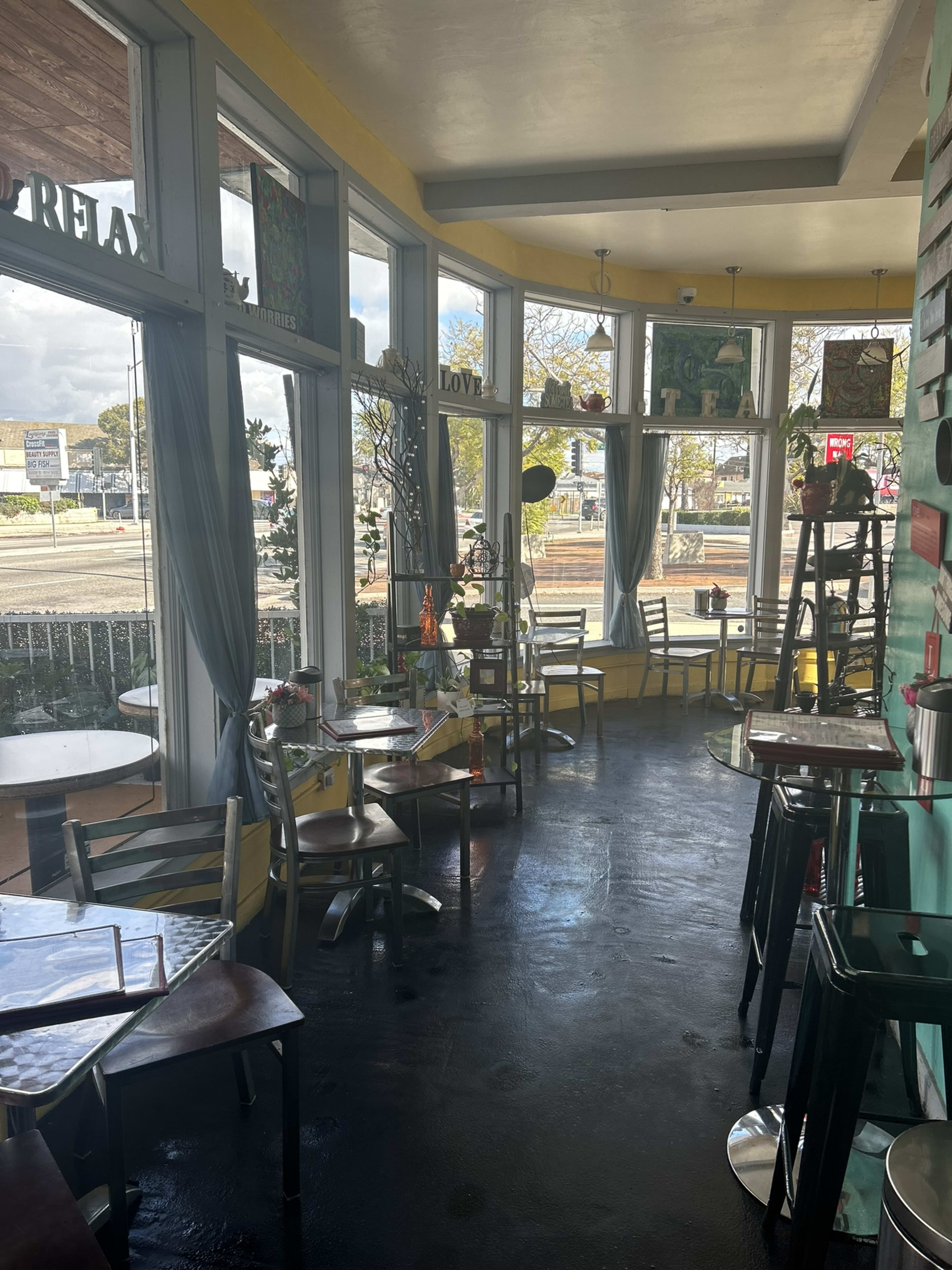 A brightly lit café interior with several tables and chairs arranged near large windows.
