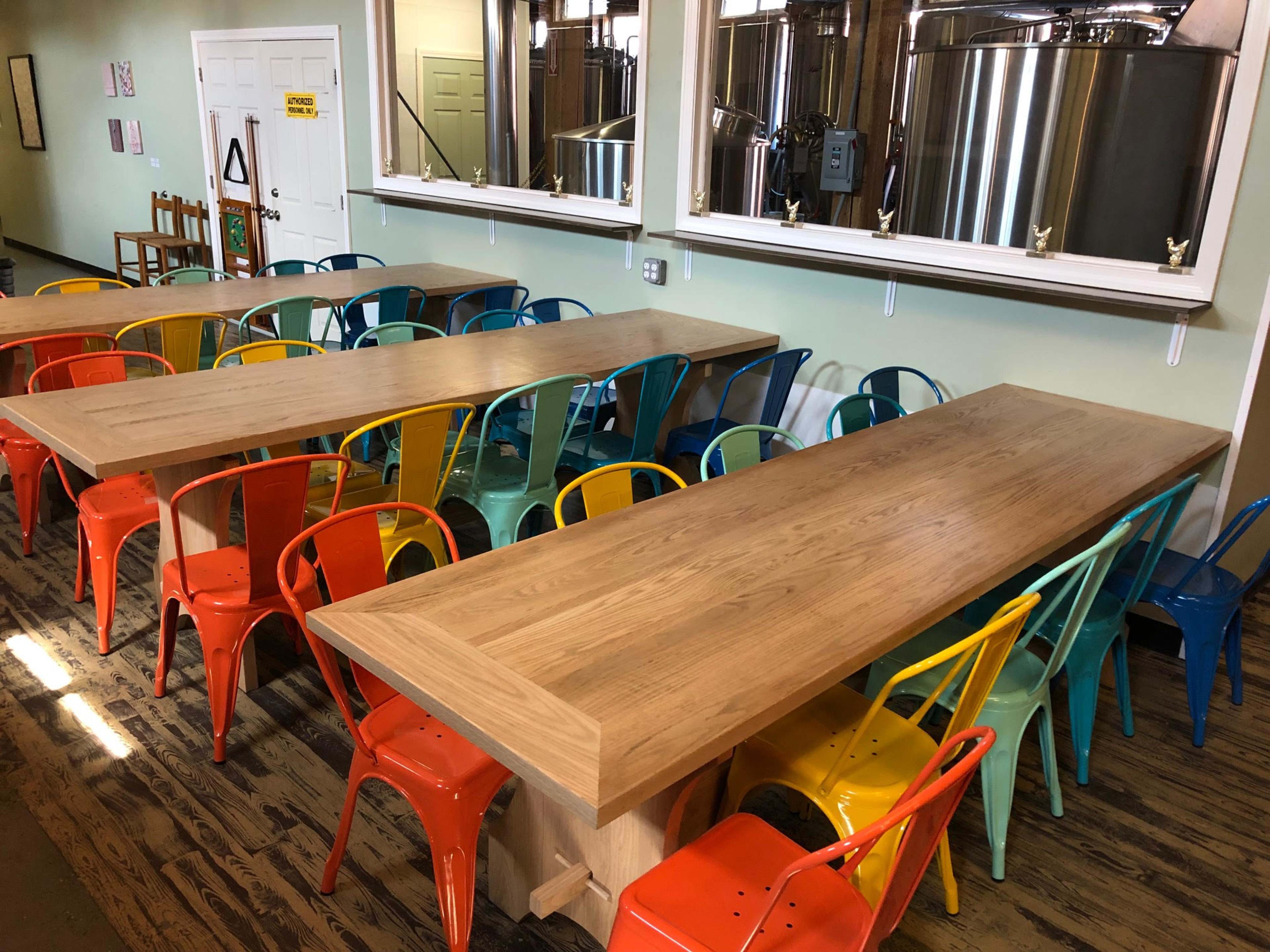 A spacious room with two long wooden tables surrounded by colorful metal chairs, reflecting a bright and airy atmosphere.