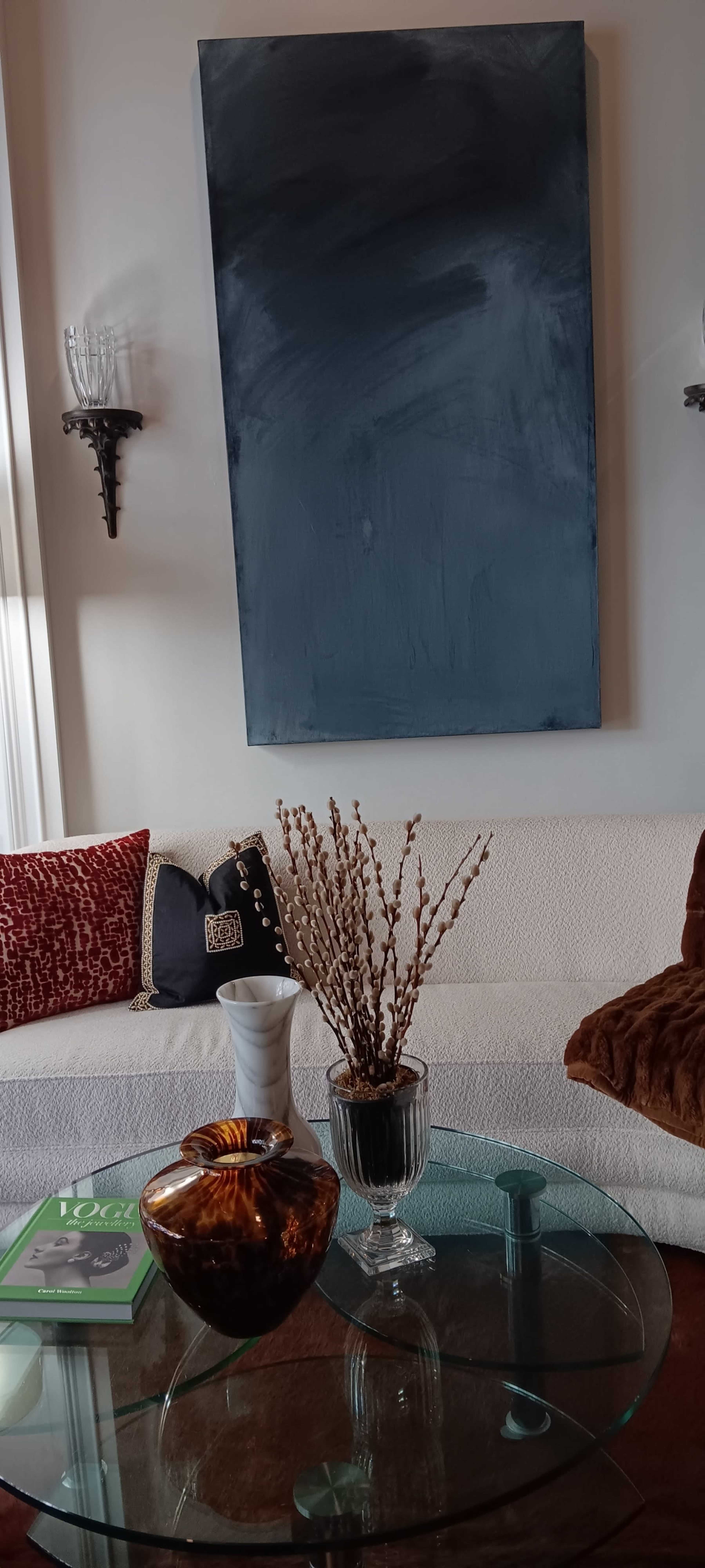 A modern living room features a white couch with decorative pillows and a coffee table displaying a decorative bowl and a vase with branches, against a backdrop of a large blue painting.