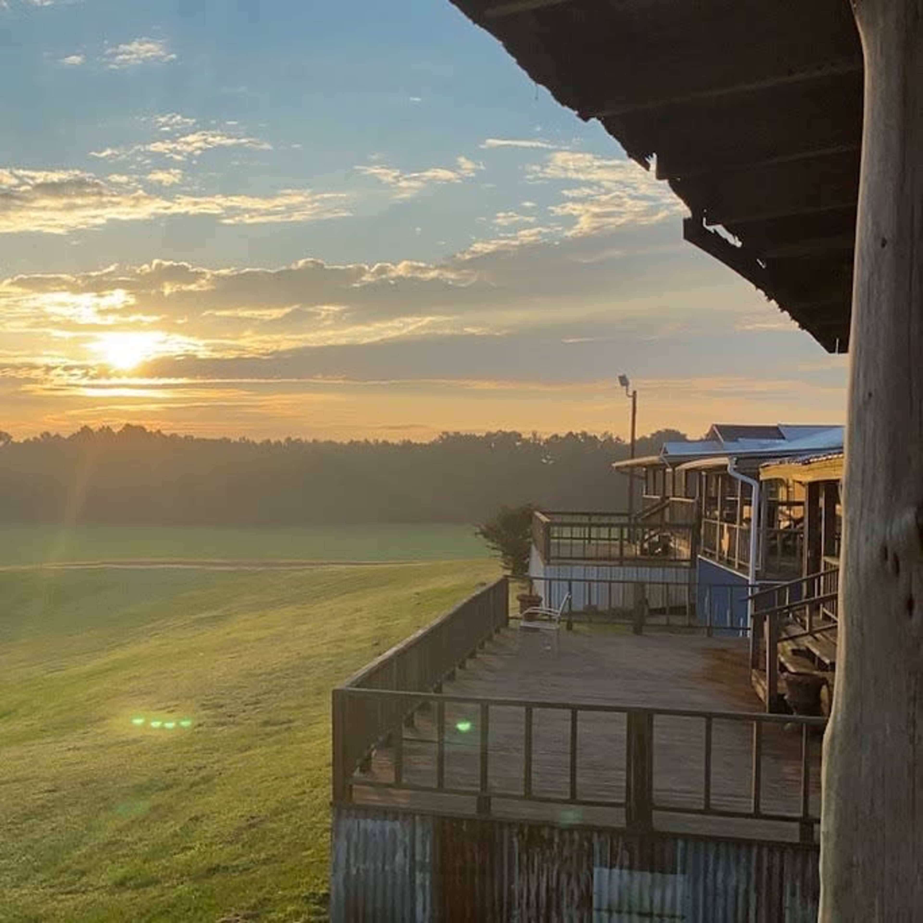 A wooden deck on a building overlooking a grassy field with a sunrise in the background.
