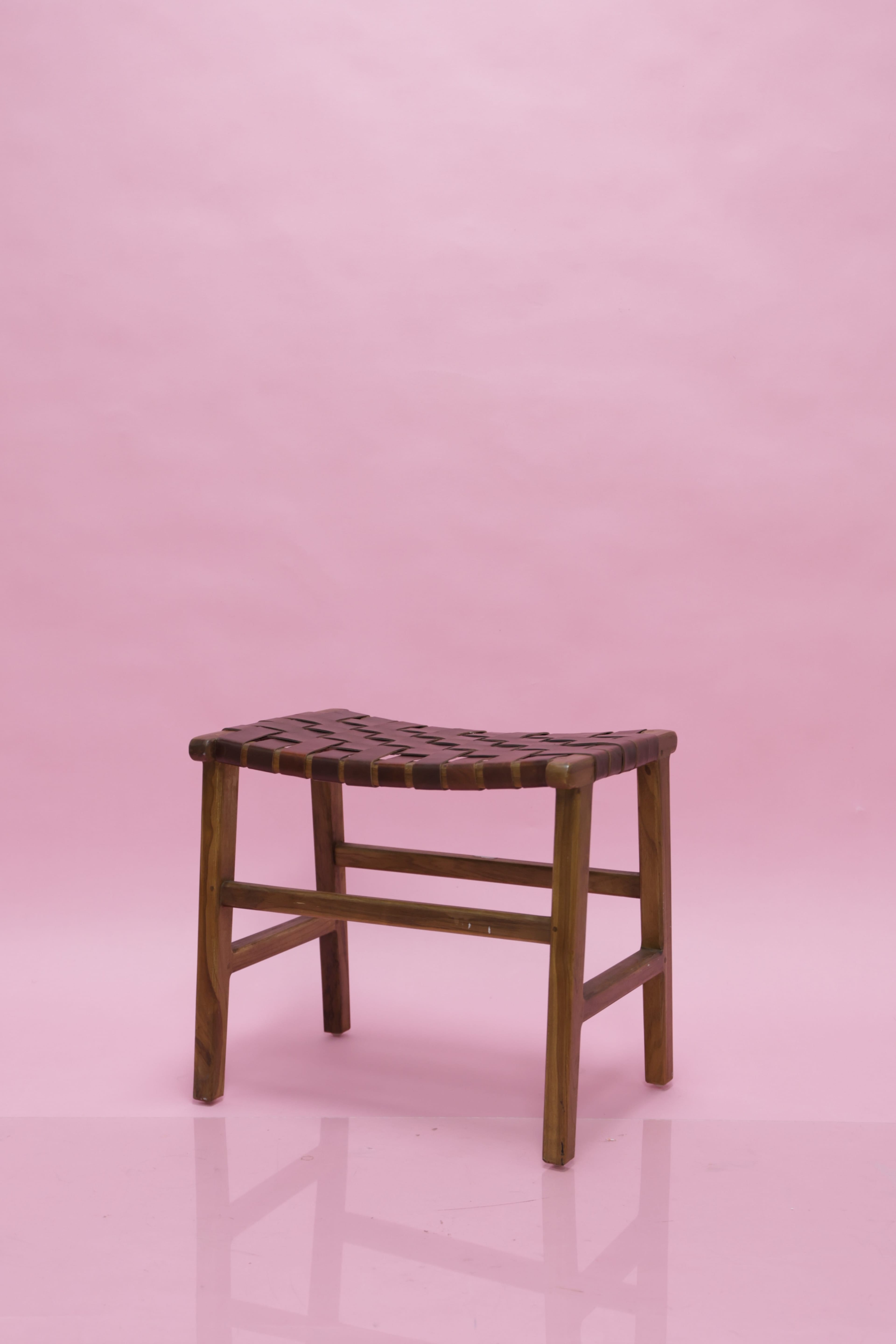 A wooden stool with a woven seat sits against a pink backdrop.