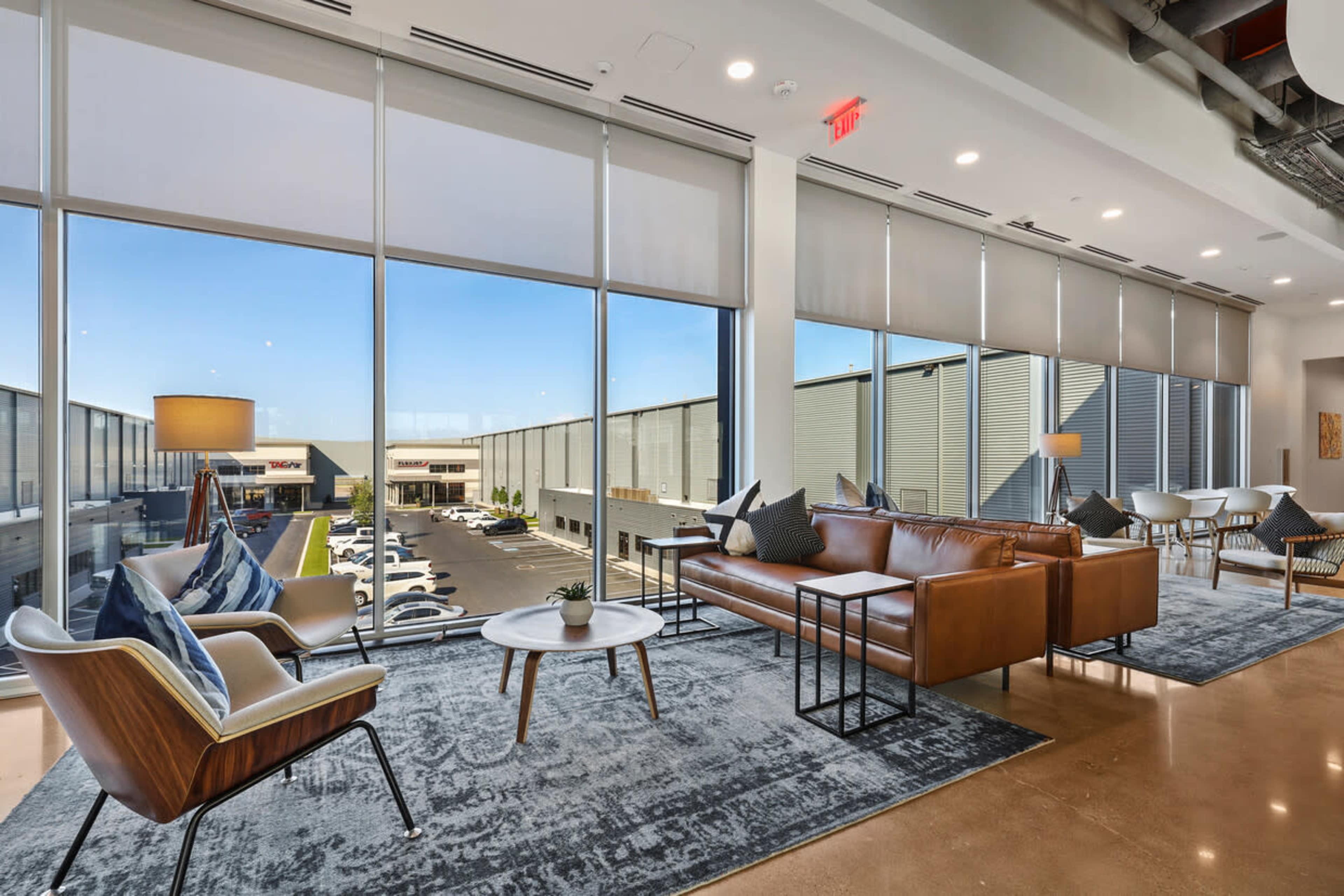 A modern lounge area features large windows, comfortable seating, and a view of an exterior parking lot filled with vehicles.