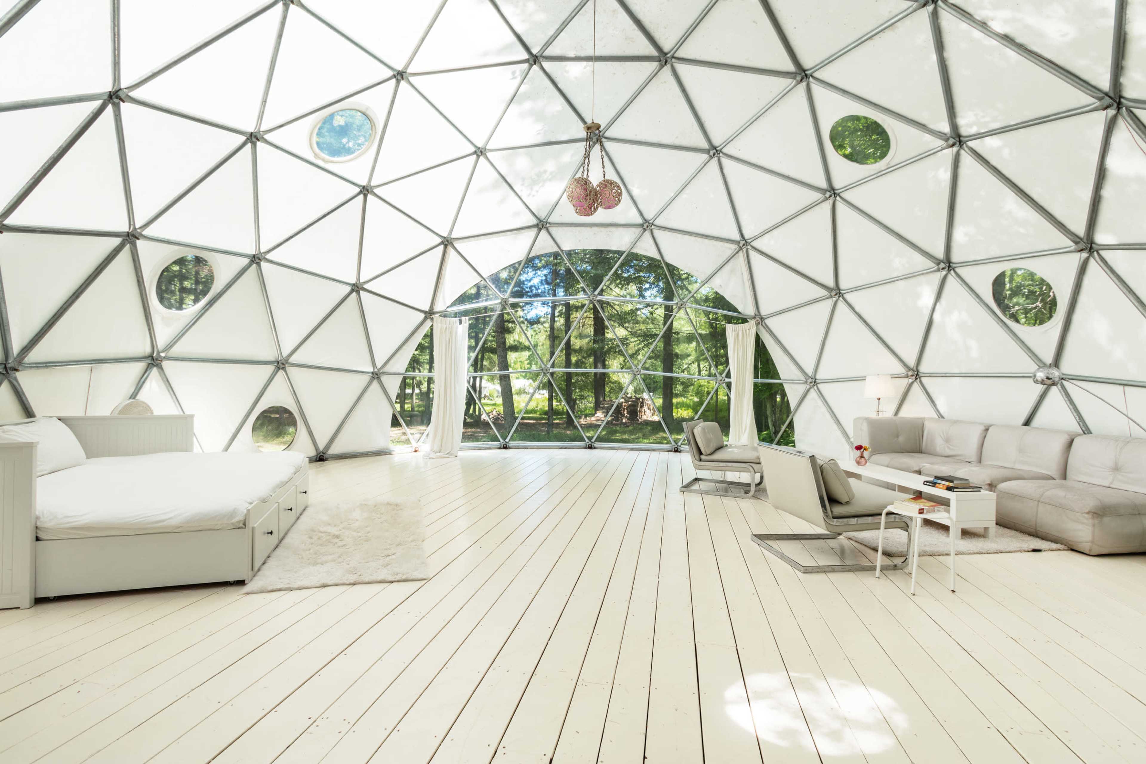 The image shows a spacious, light-filled geodesic dome with a seating area and large windows overlooking a green landscape.