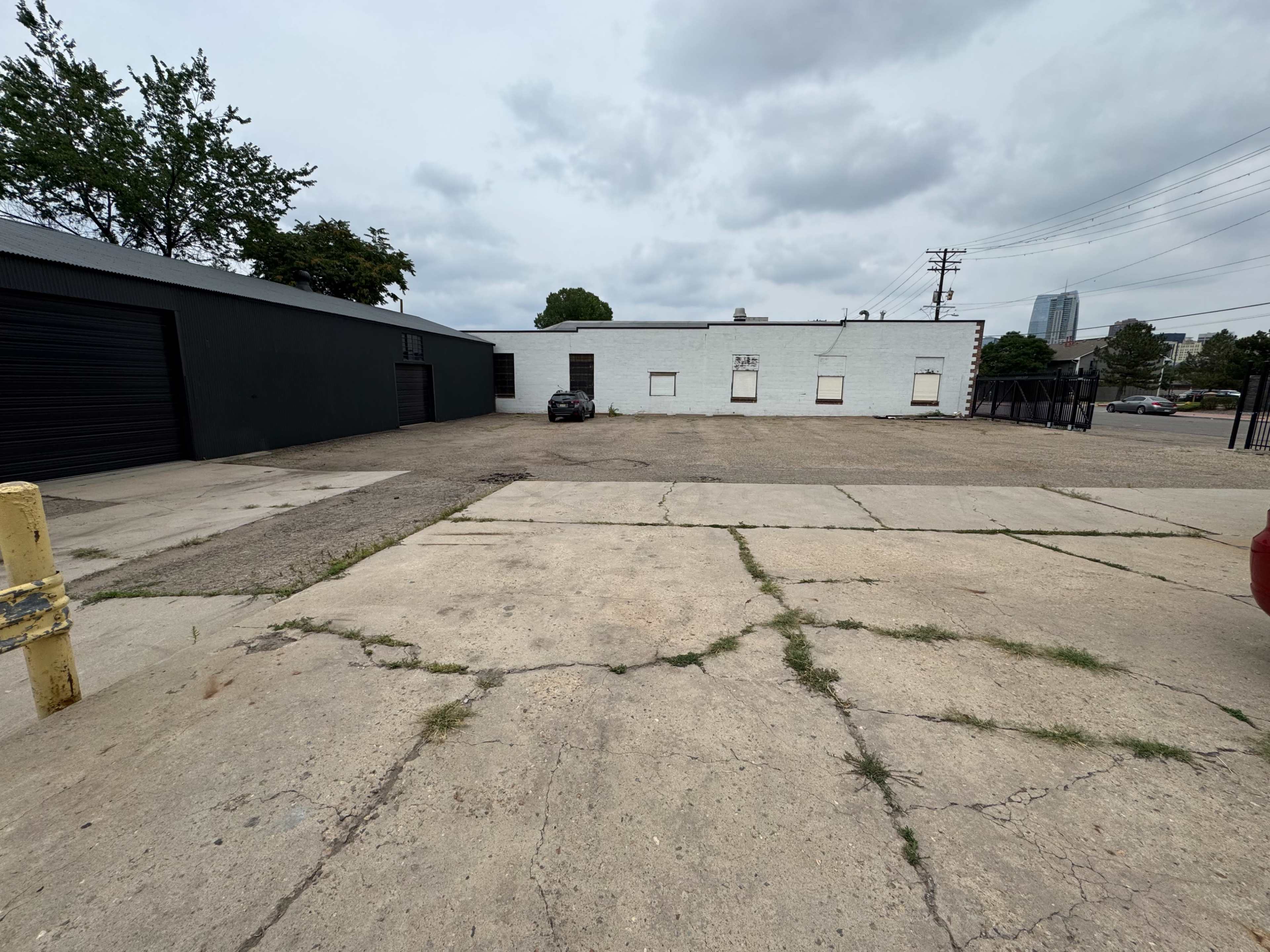 The image shows a flat, paved area with a partially visible white building and a black garage on the left, under a cloudy sky.