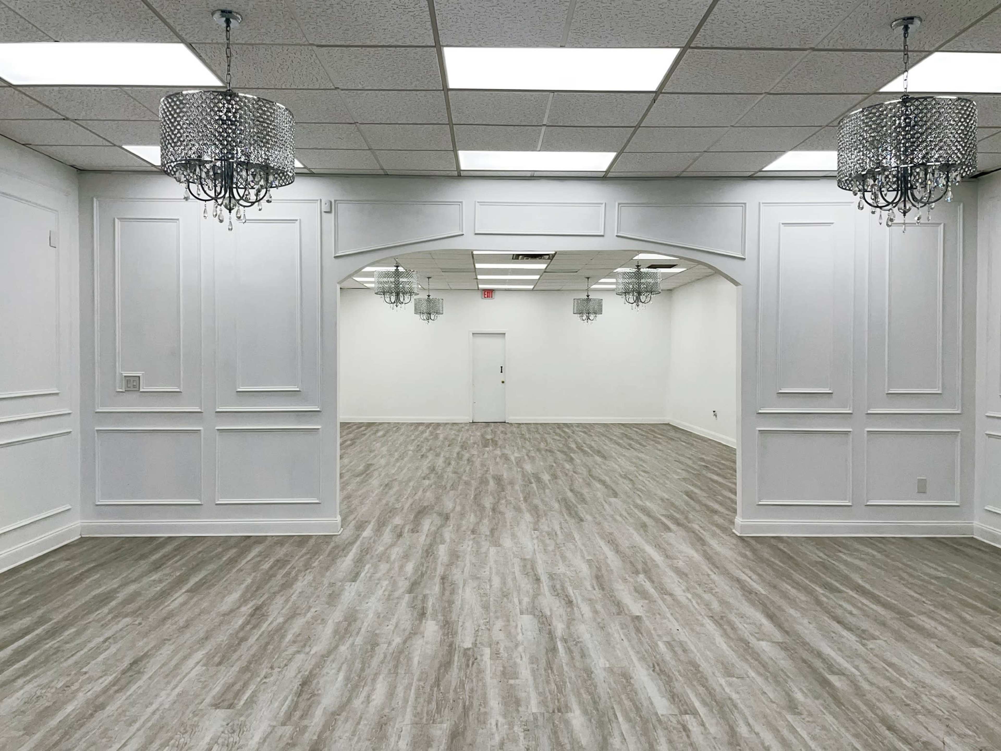 The image shows a large, well-lit room with white walls, a wooden floor, and several decorative chandeliers hanging from the ceiling.