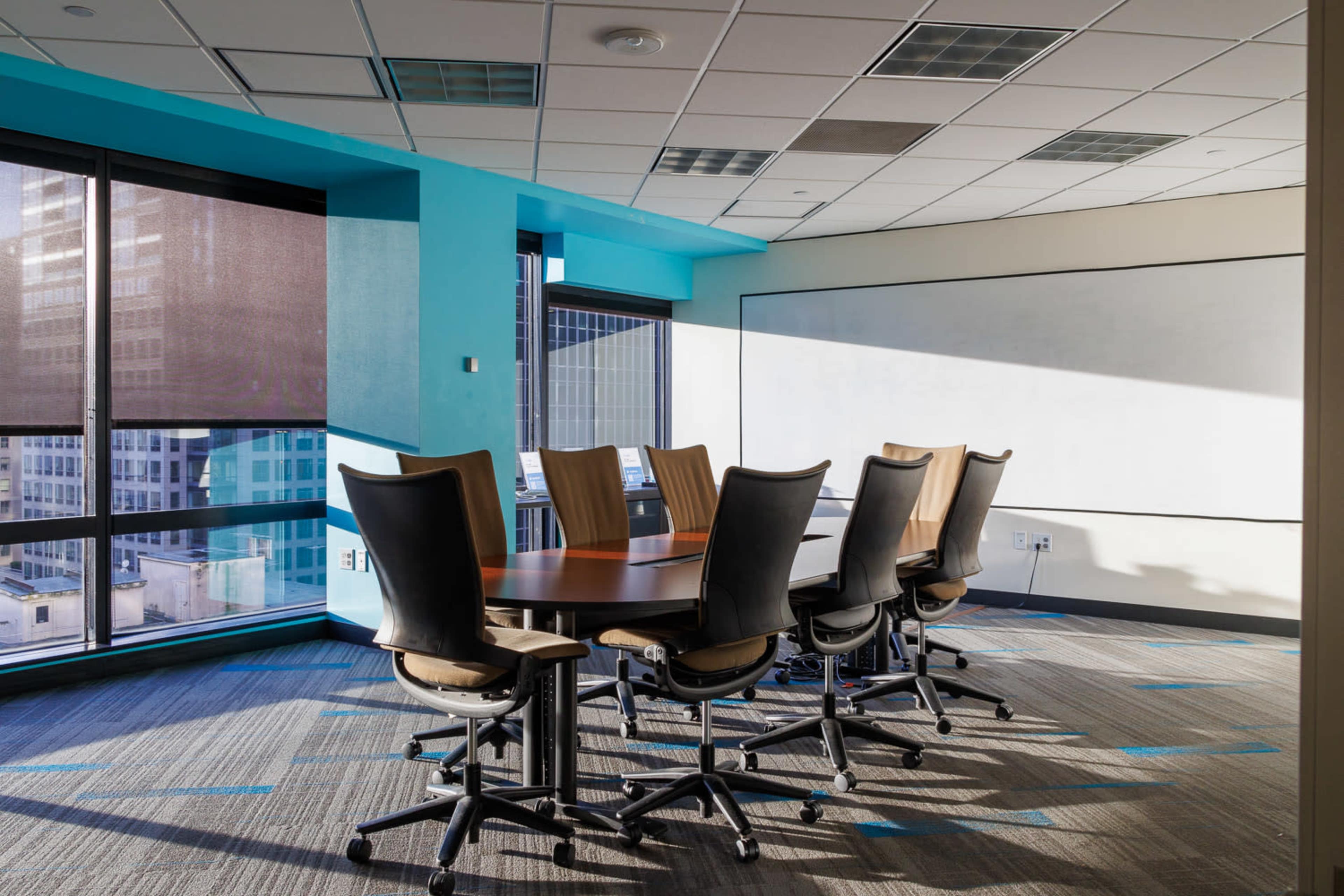 A modern conference room features a large round table surrounded by ergonomic chairs, with windows allowing natural light to illuminate the space.