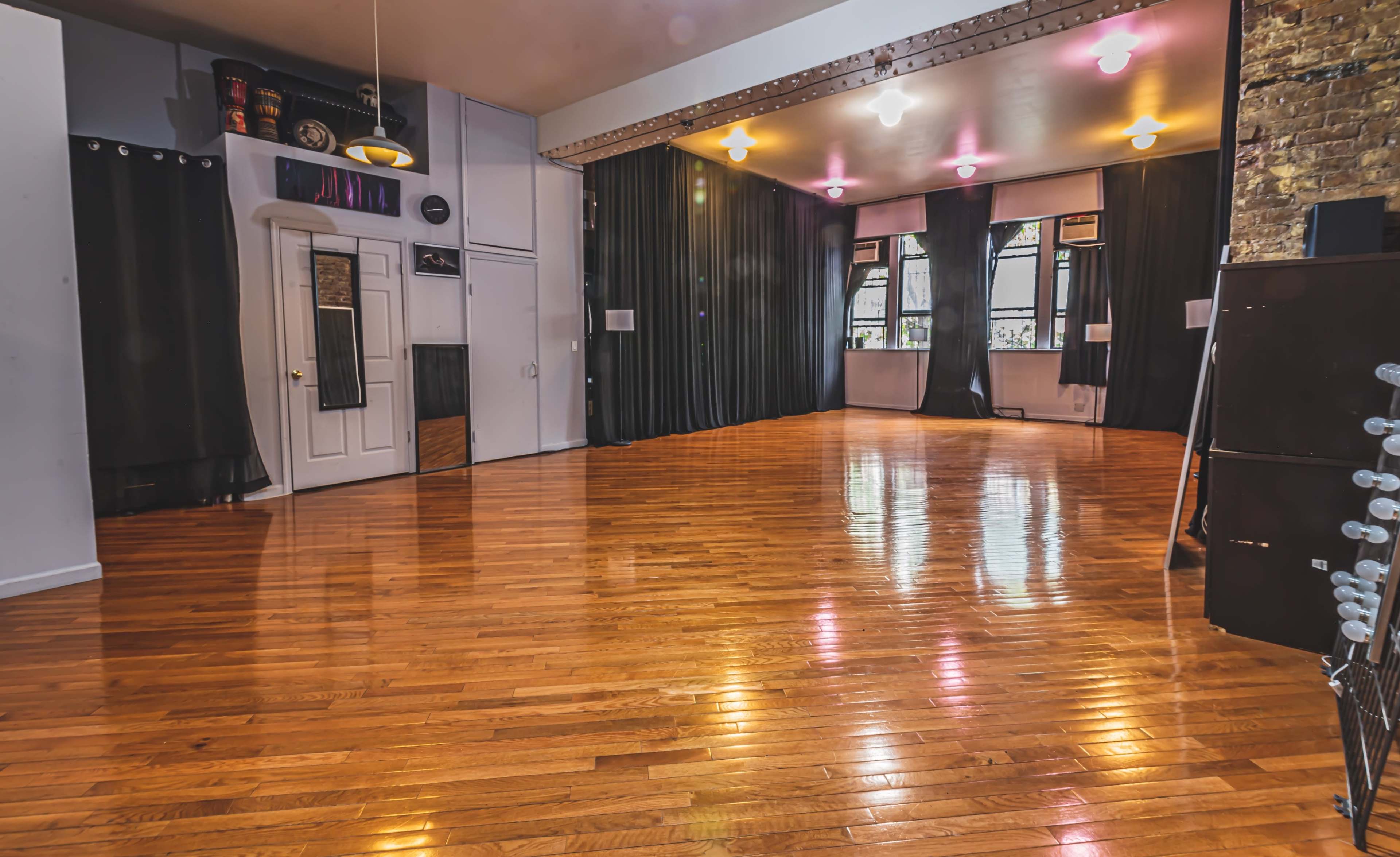 A spacious room with polished wooden floors, black curtains, and a large mirror on one wall.