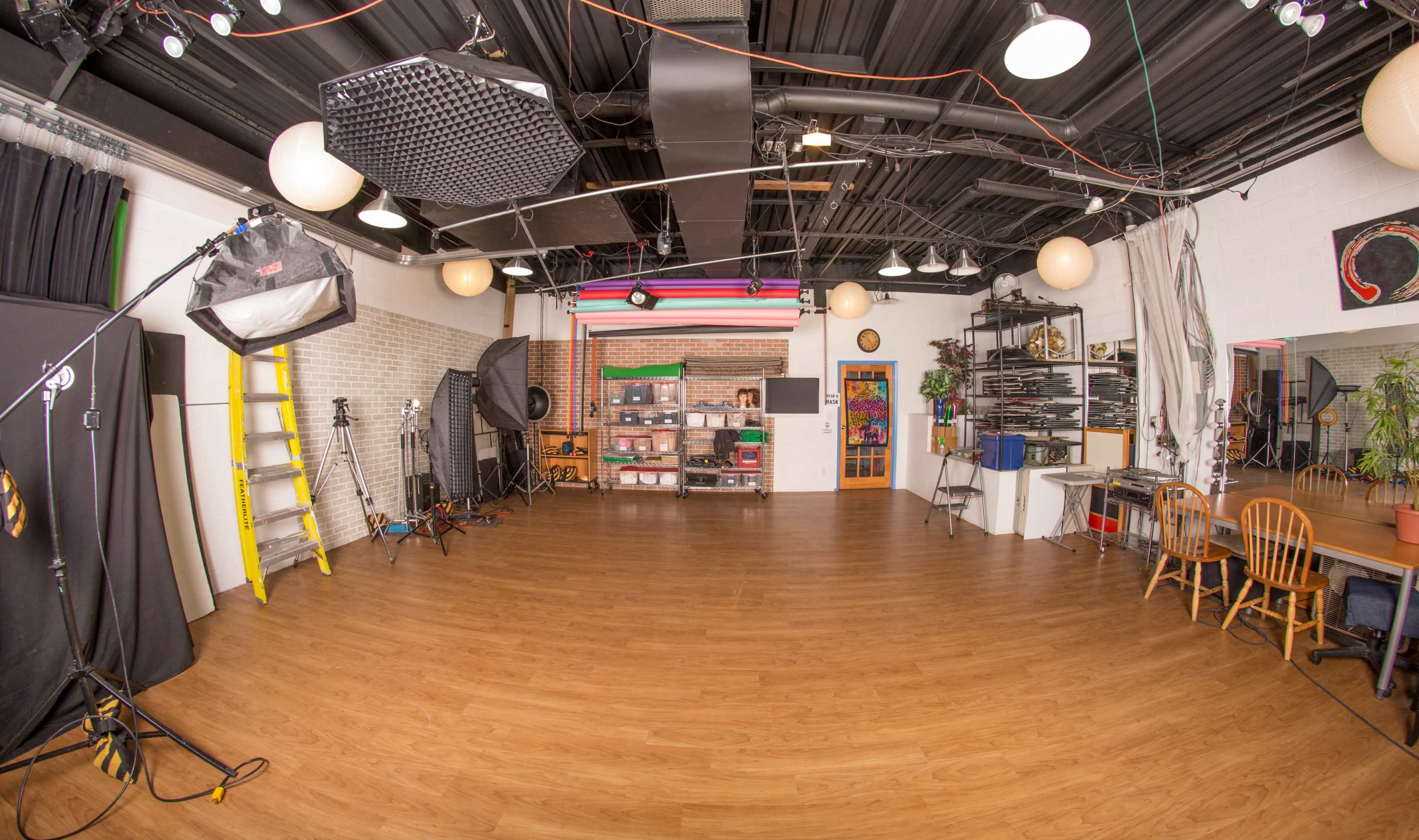 A spacious photography studio features various lighting equipment, props, and a wooden floor.