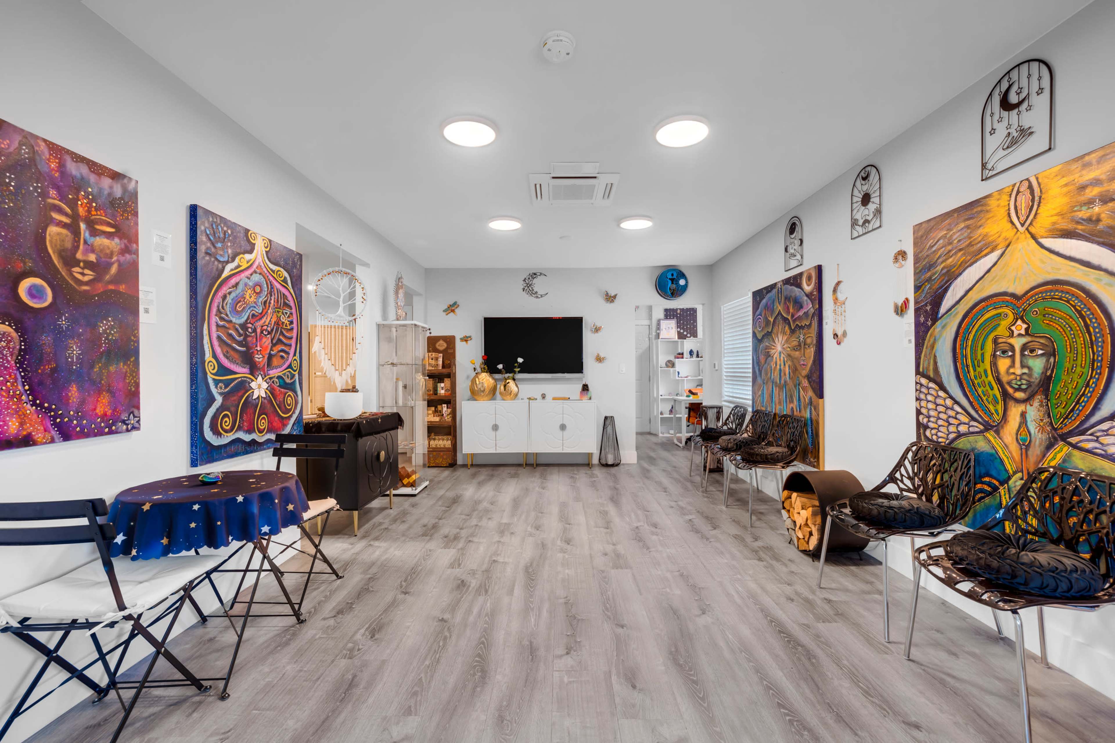 The image shows a colorful room decorated with vibrant artwork featuring faces and symbols, furnished with chairs and a television.