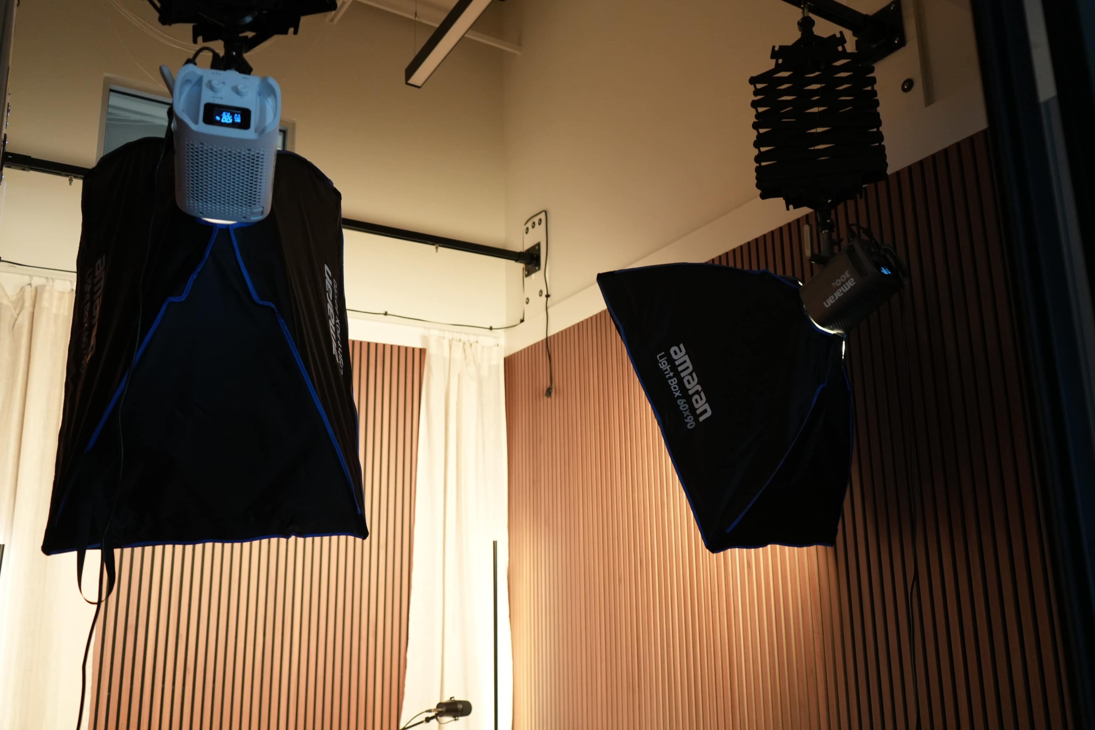 The image shows two studio lights suspended from the ceiling in a room with wooden paneling and curtains.