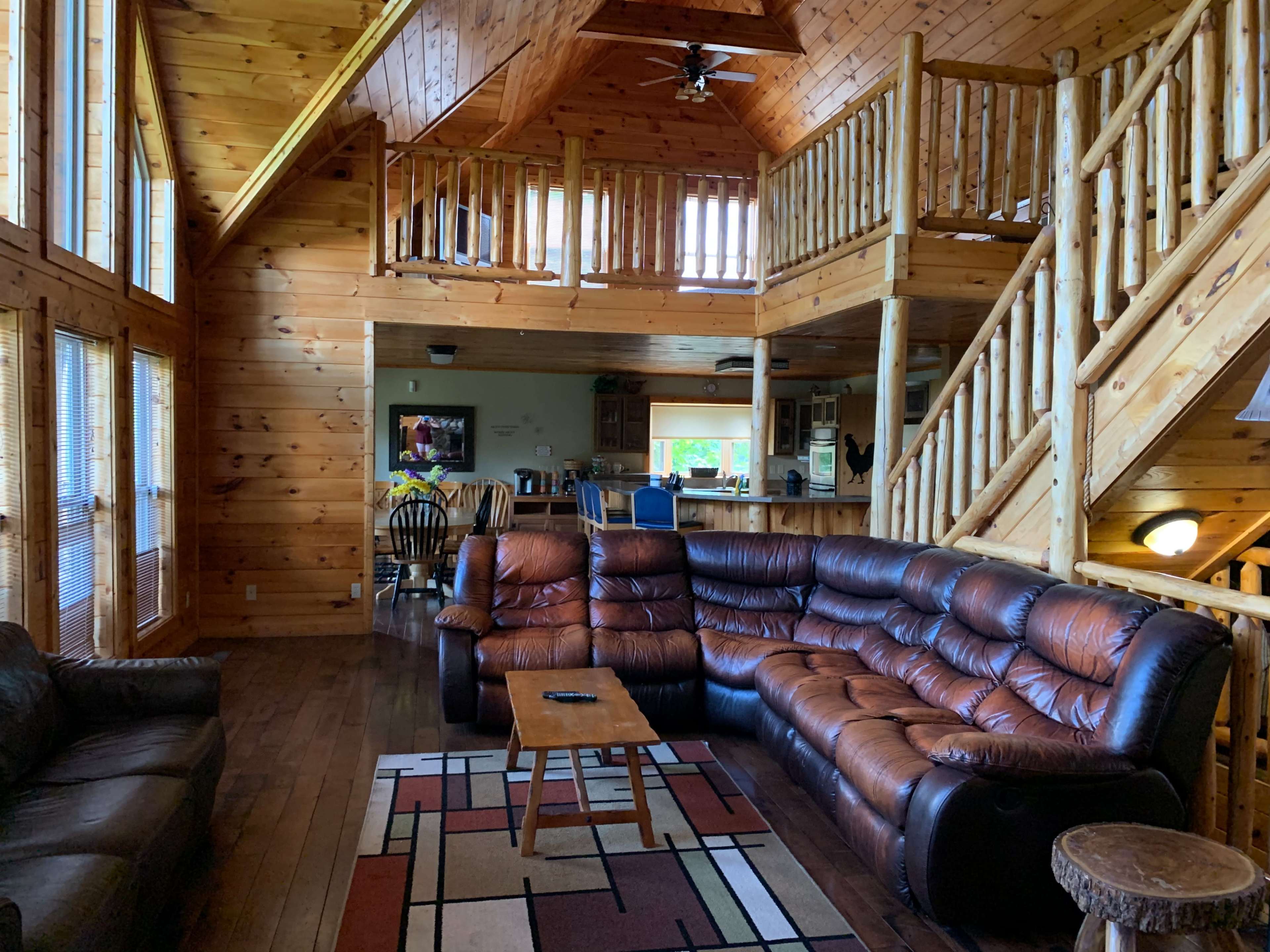 A large wooden cabin interior with a couch, coffee table, and two levels featuring a staircase and a kitchen area.