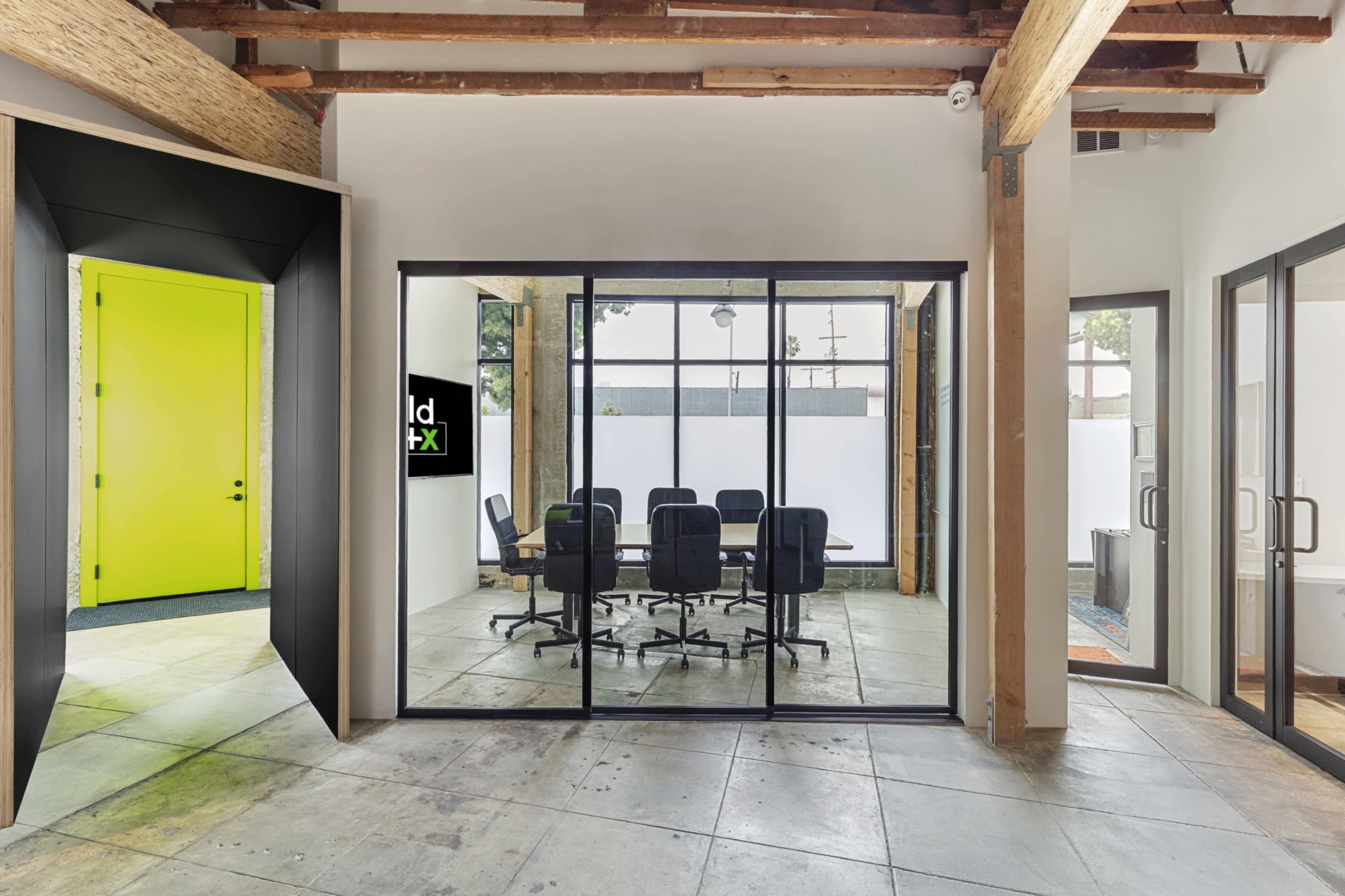 The image shows a modern office space featuring glass walls enclosing a conference room, with a bright green door leading to another area.