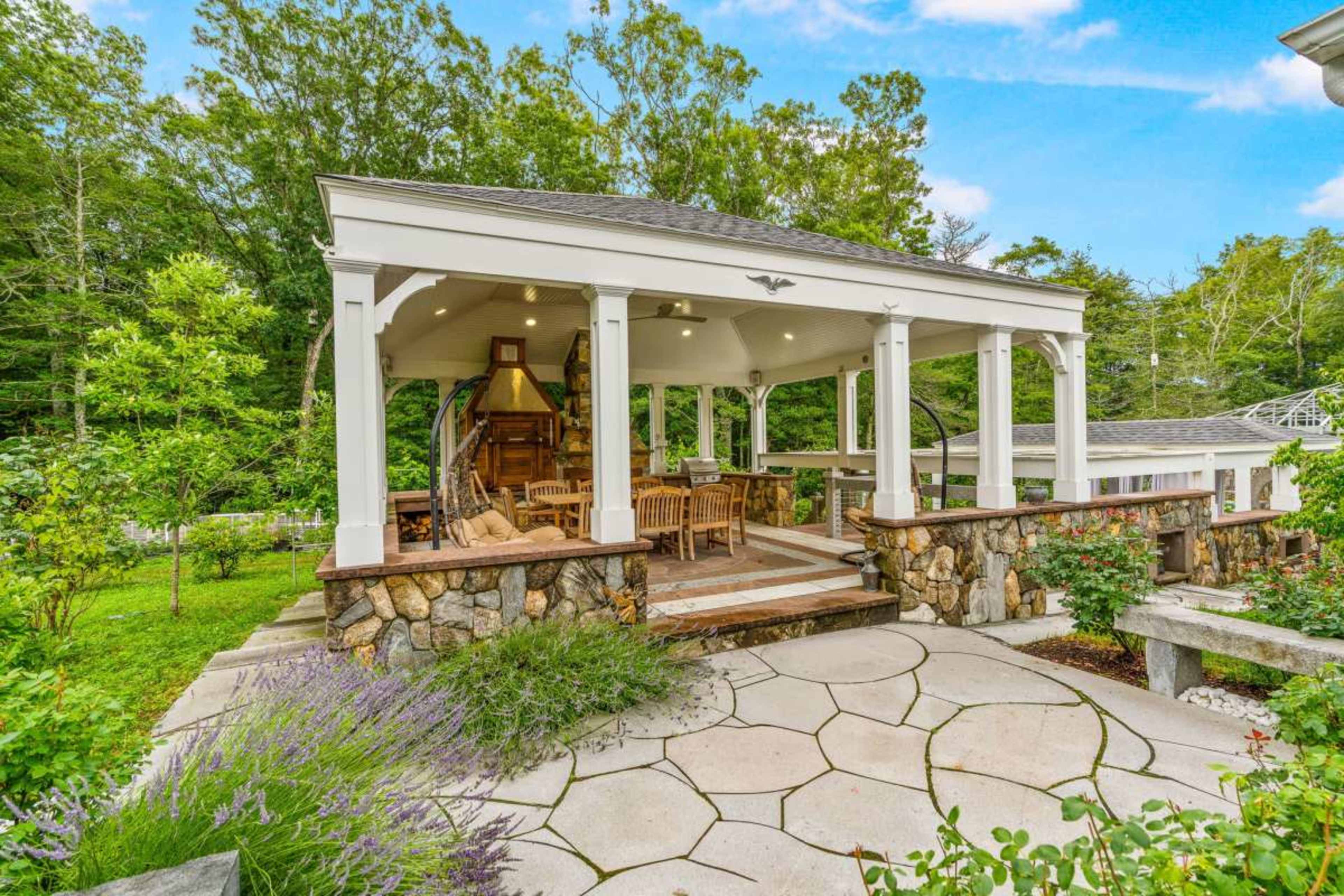 A gazebo with a wooden structure and large seating area is surrounded by stone walls and landscaped greenery.