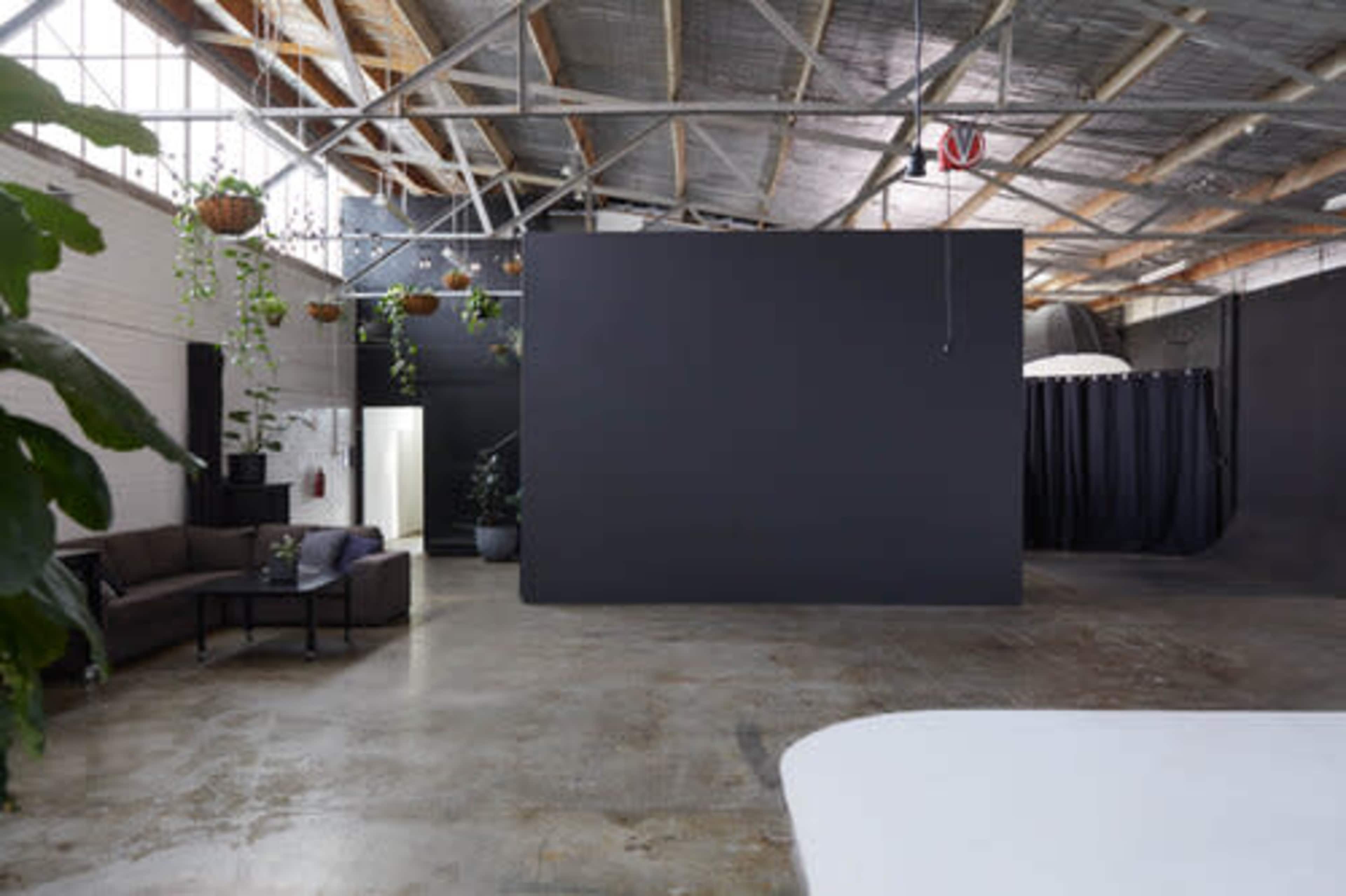 A spacious, industrial-style room with a concrete floor, a large black wall, and a seating area featuring a sofa and coffee table.