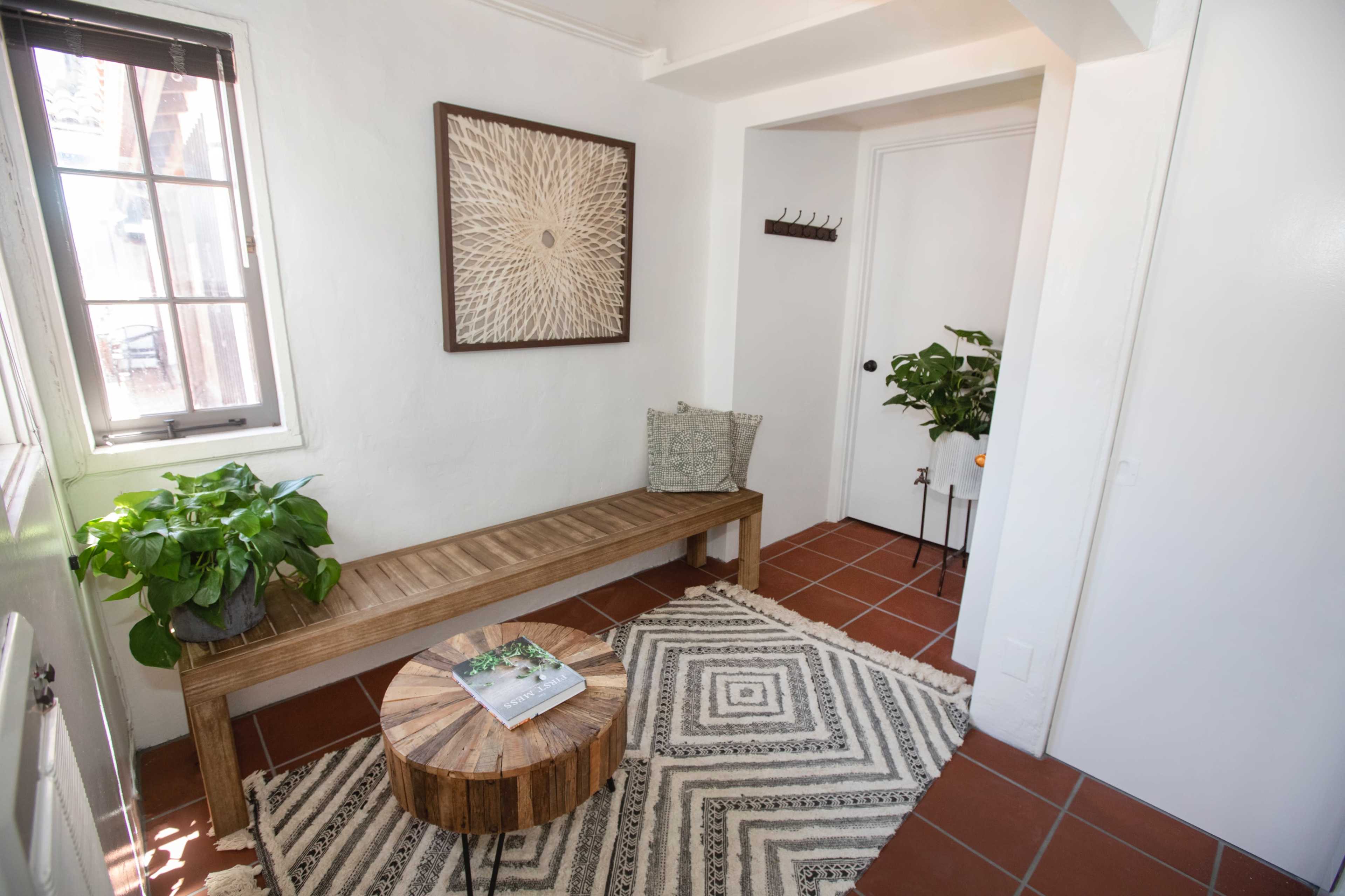 A hallway with a wooden bench, a round wooden table, a patterned rug, and a plant in a corner.