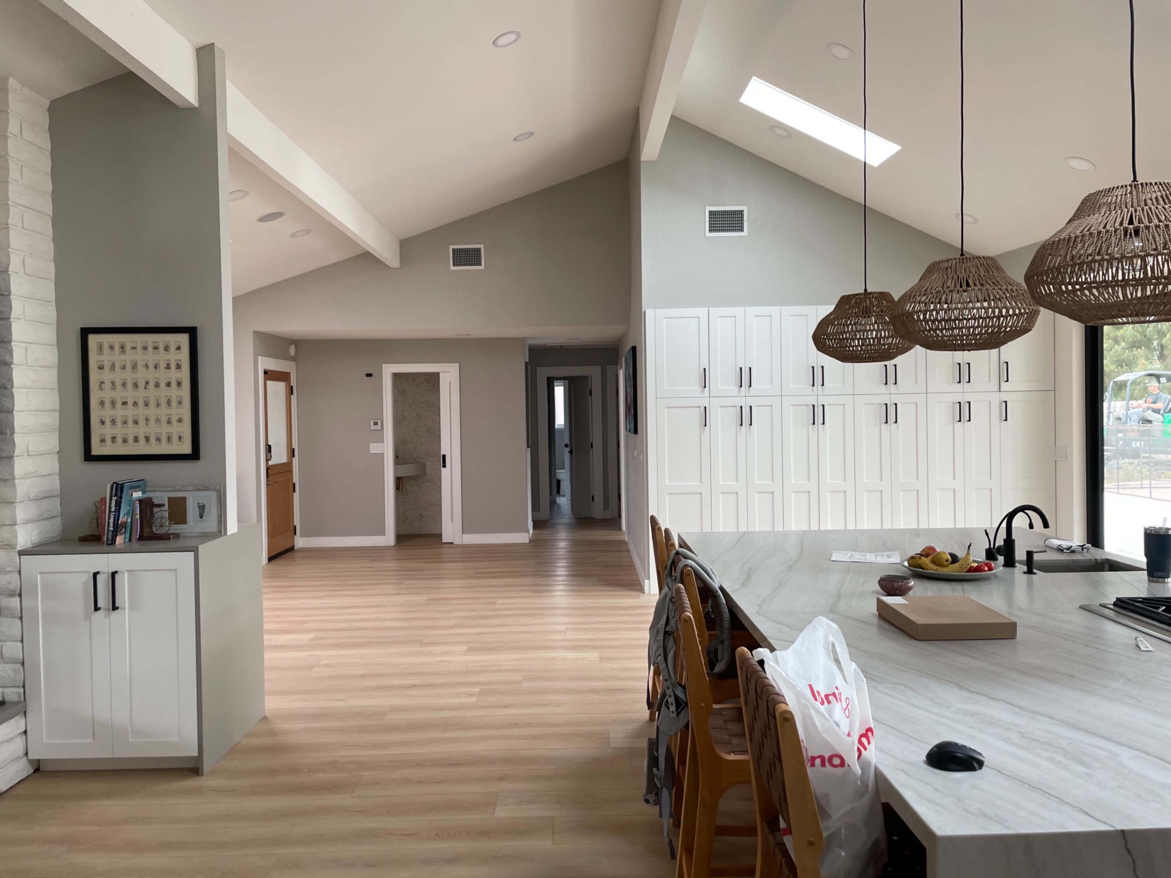 The image shows a modern open-concept living space with a kitchen area, dining table, and a hallway leading to additional rooms.