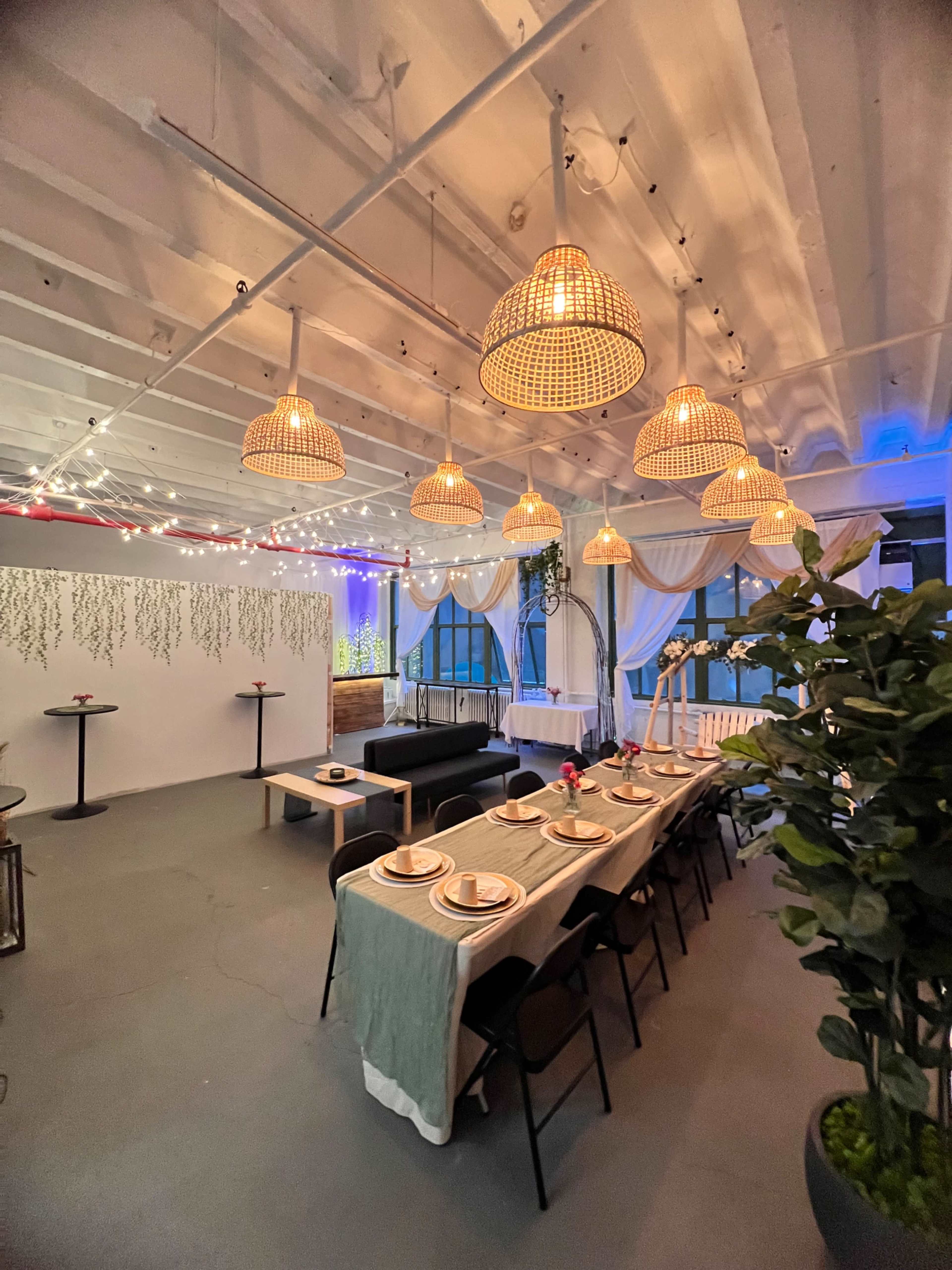 A well-lit dining area with a long table set for a meal, surrounded by decorative hanging lamps and plants.