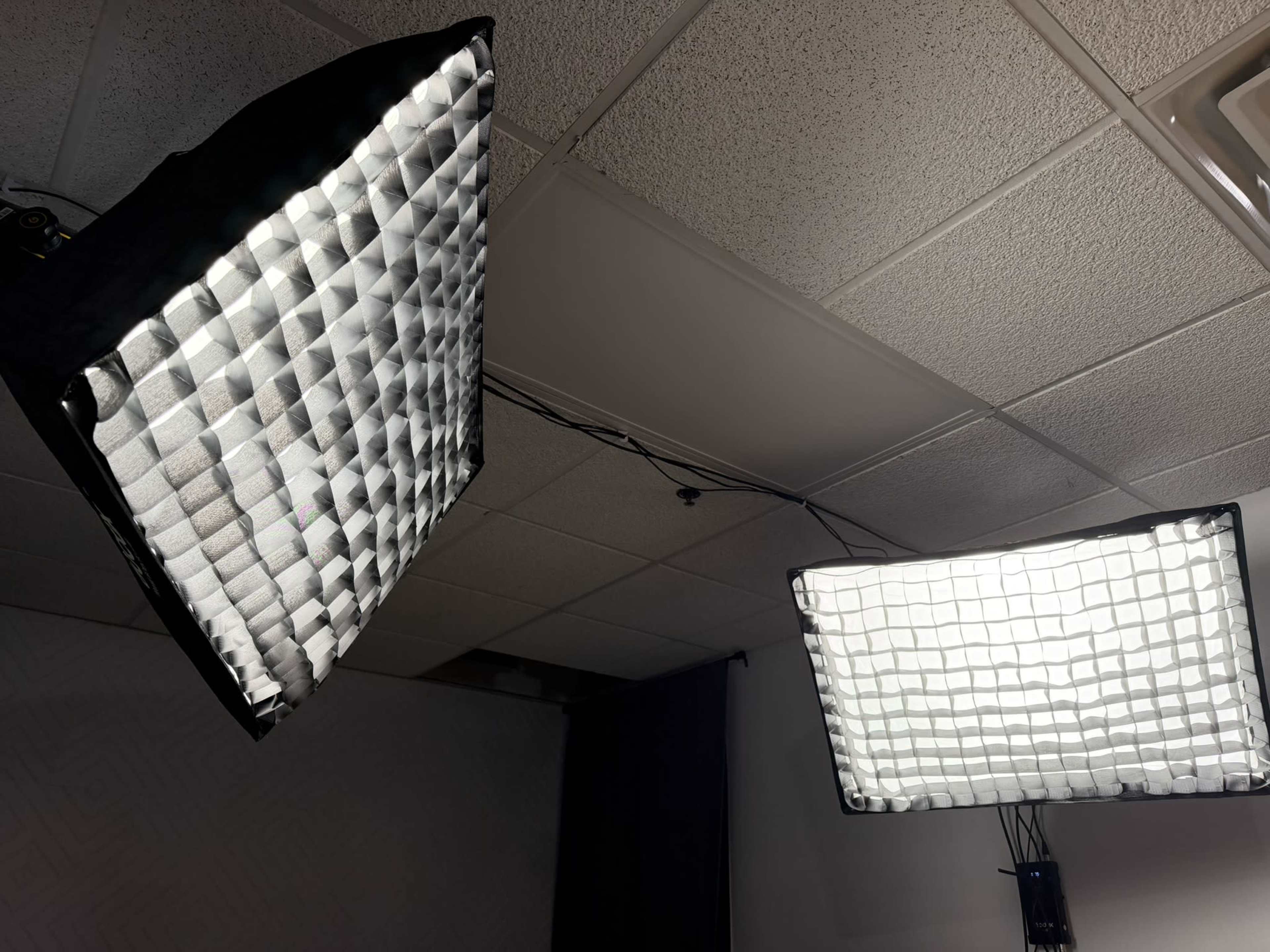 The image shows two large softbox lights mounted on the ceiling, illuminating a room with drop ceiling tiles.