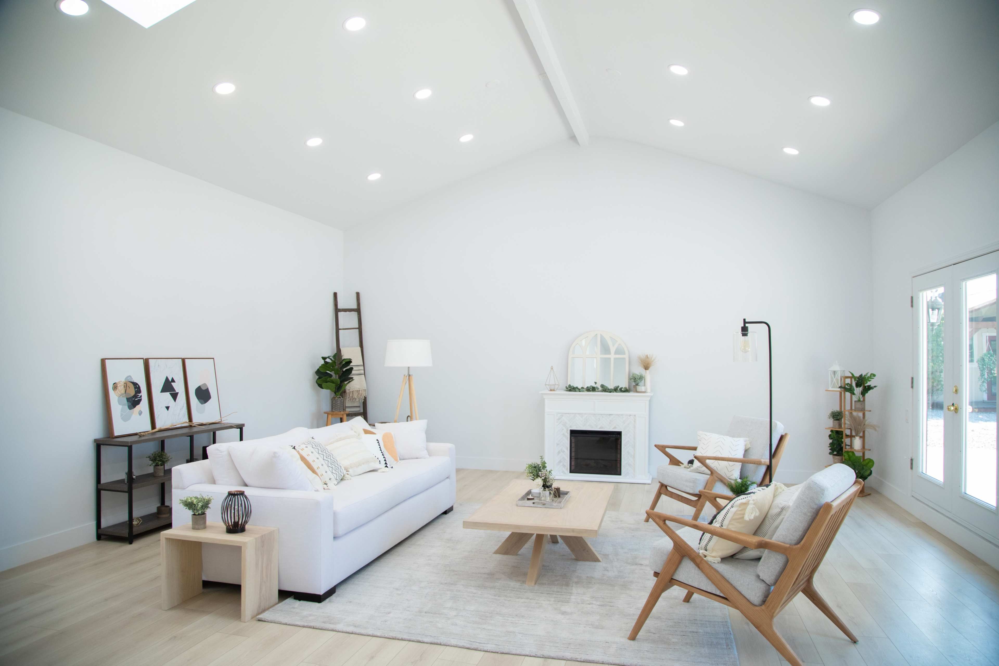 A modern living room features a white sofa, wooden chairs, a coffee table, and a minimalist fireplace, with wall art and plants accenting the space.