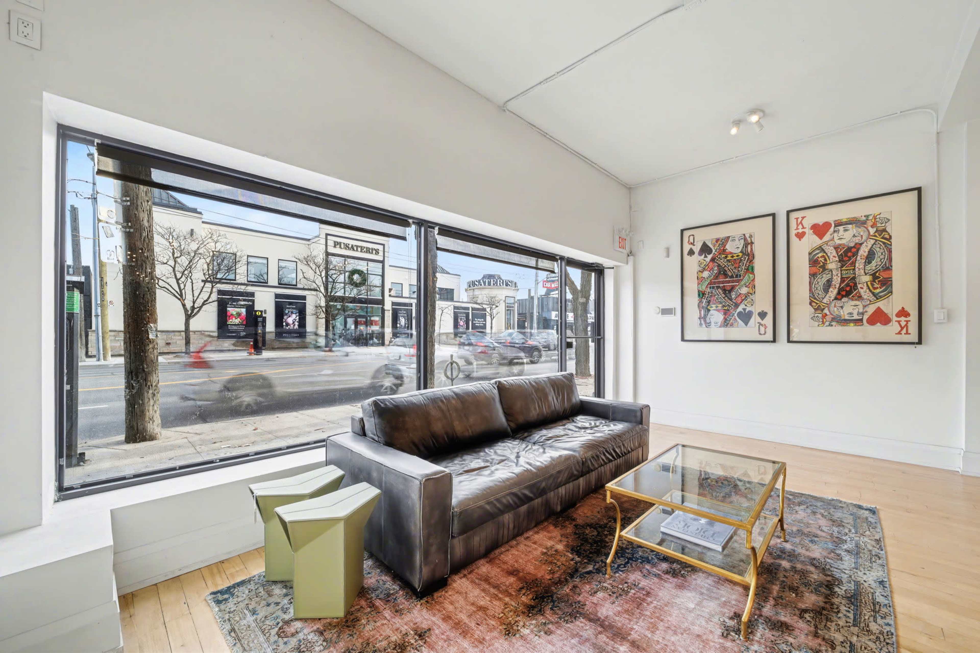 A modern living space features a dark leather sofa and a glass coffee table, with large windows showing a street view outside.
