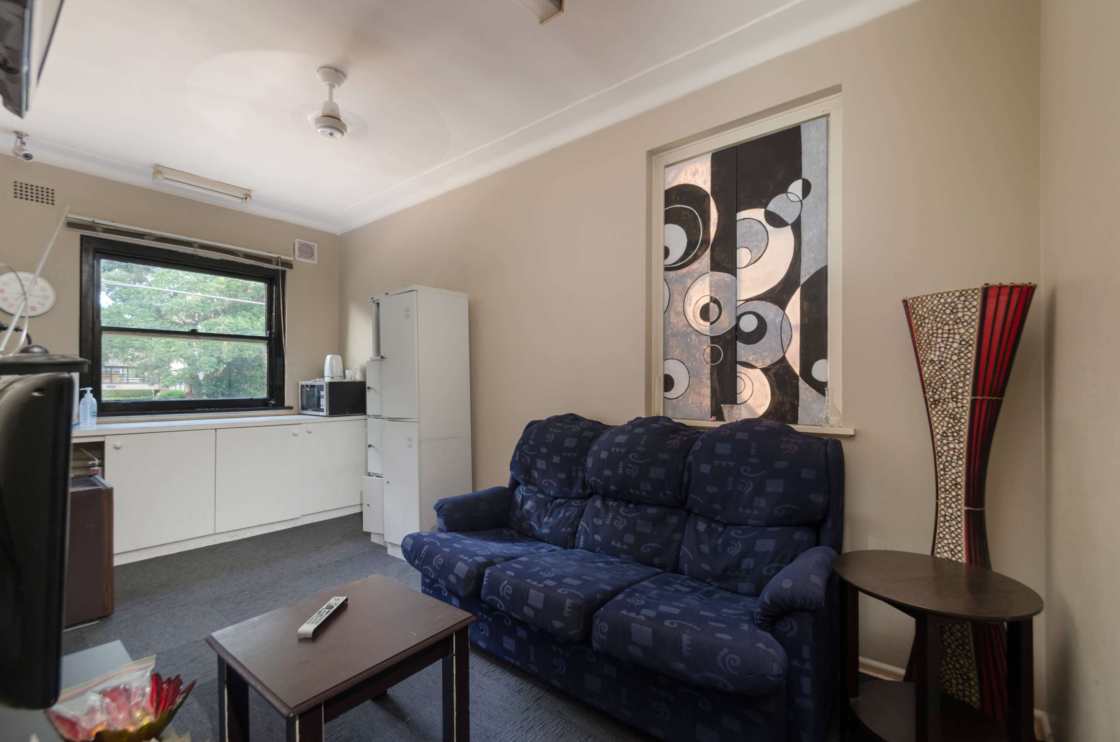 A small living area with a blue sofa, a wooden coffee table, and a kitchenette in the background.
