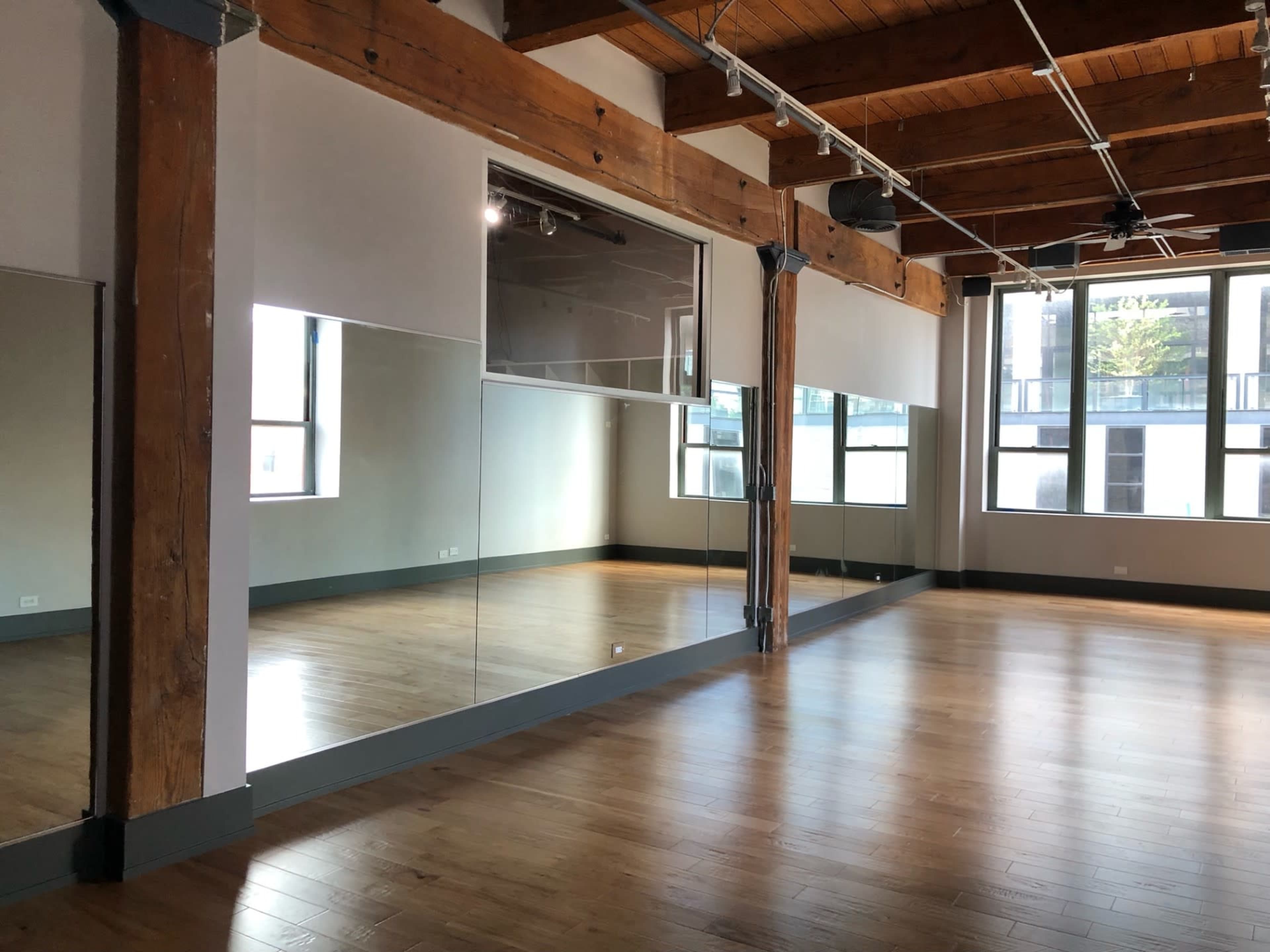 A spacious room with wooden beams, large windows, and a wall of mirrors reflecting the interior.