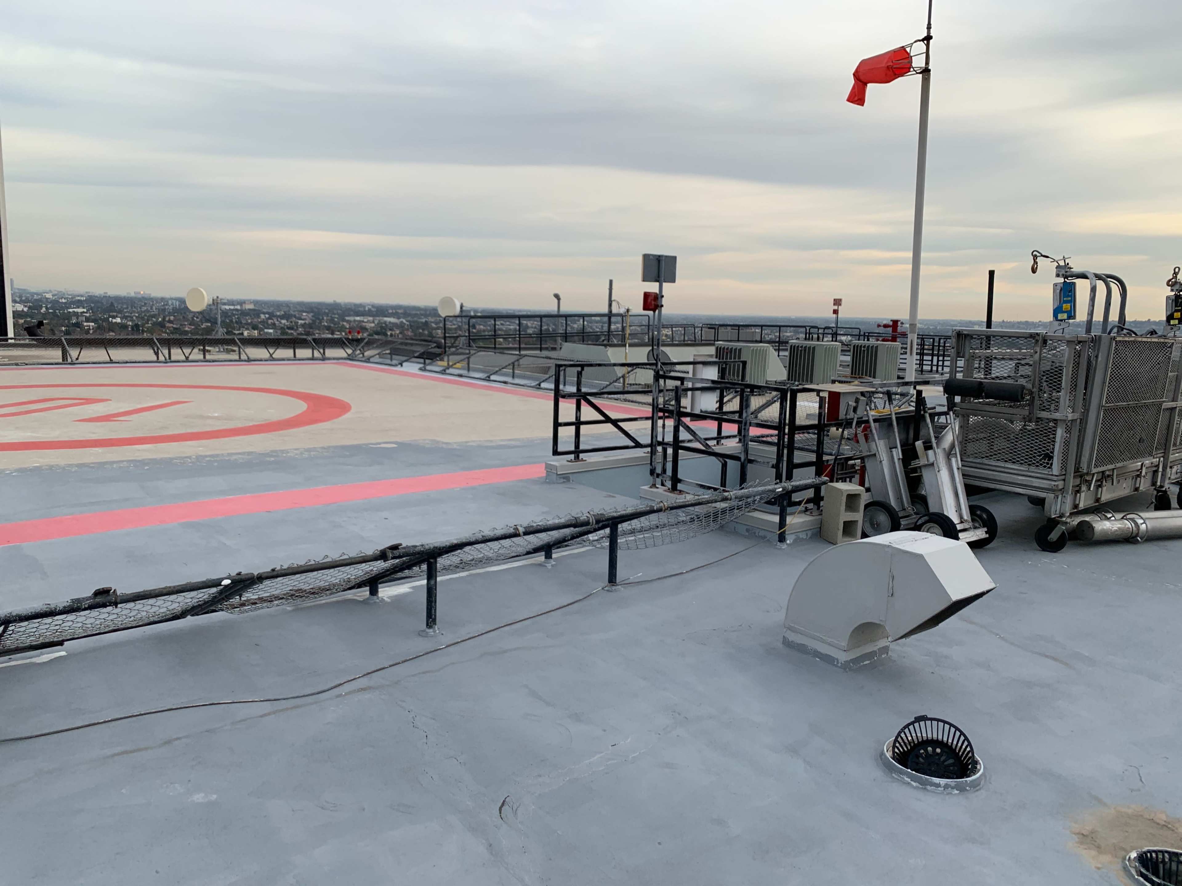 A helipad with a red stripe and various equipment, including antennas and a wind flag, set against an overcast sky.