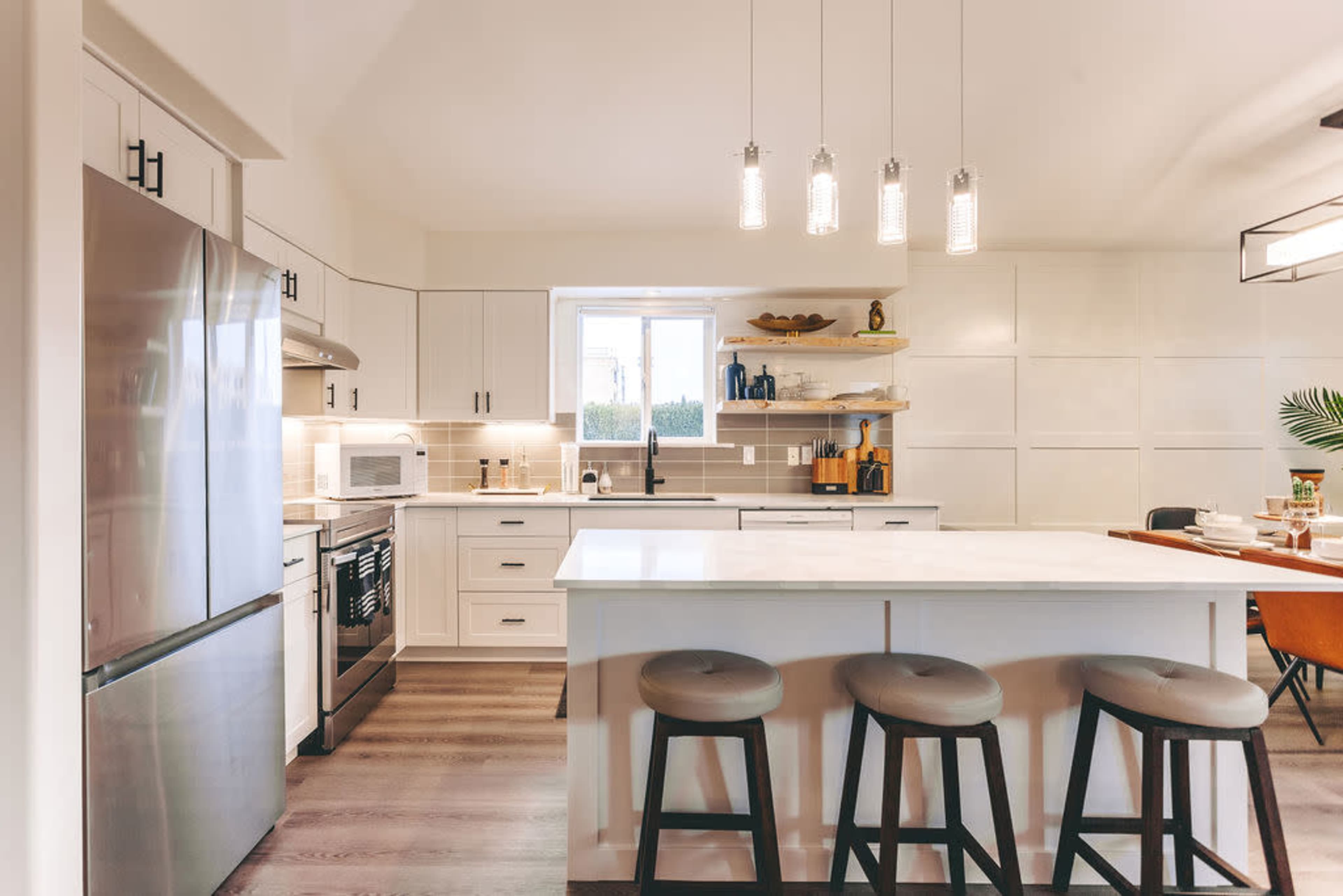 The image shows a modern kitchen with white cabinetry, a large island, and pendant lighting above the bar stools.