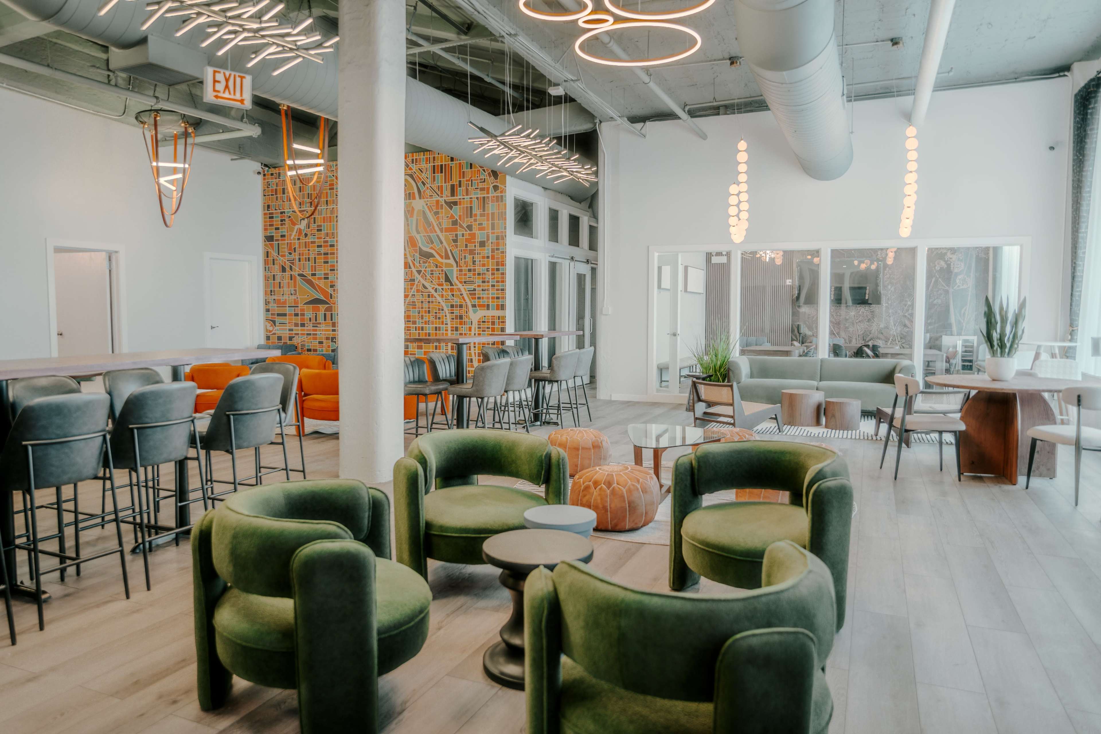 A modern lounge area featuring green armchairs, a mix of seating options, a patterned accent wall, and large windows.