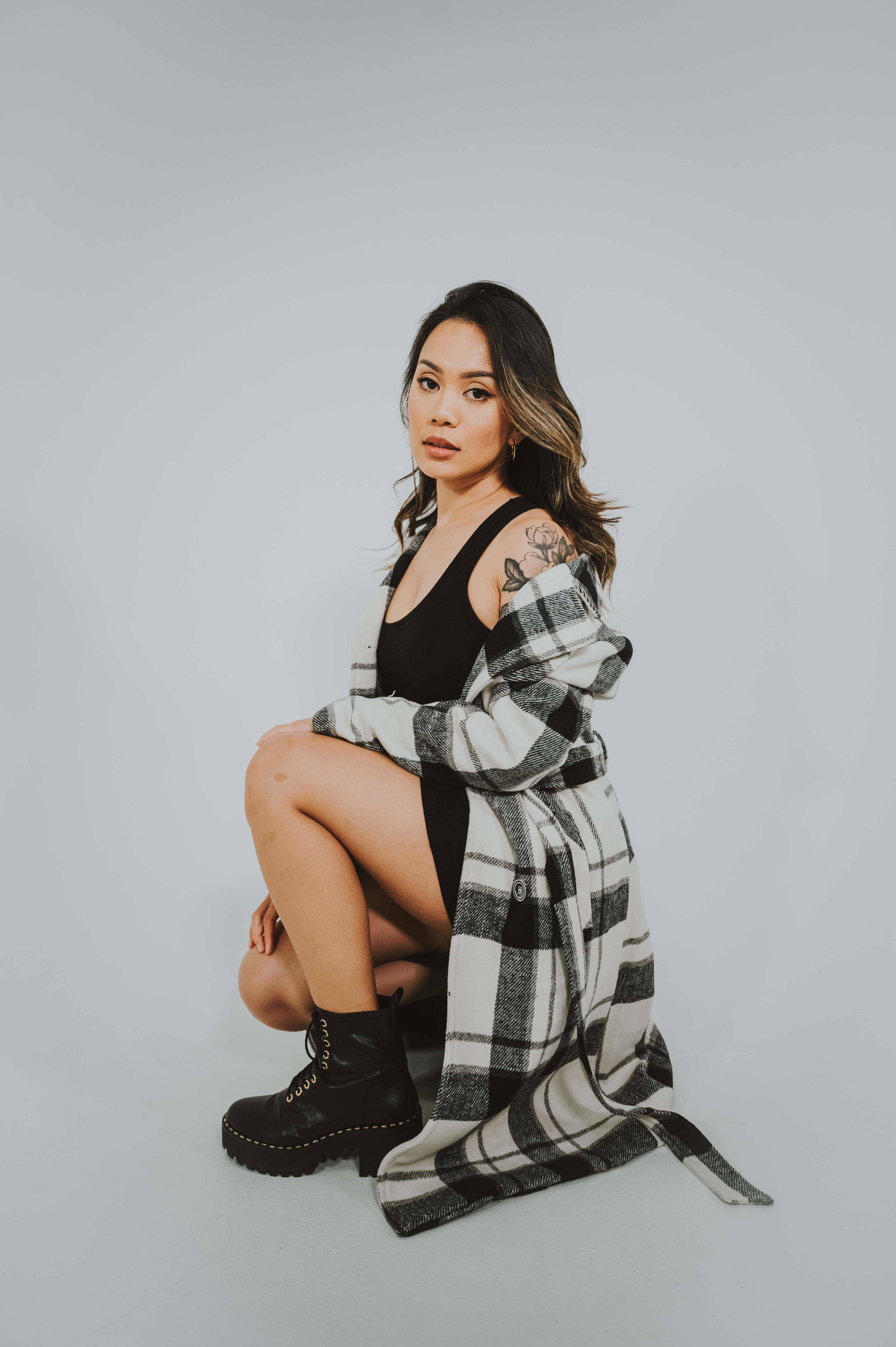 A woman sitting on the ground wearing a black and white checkered coat.