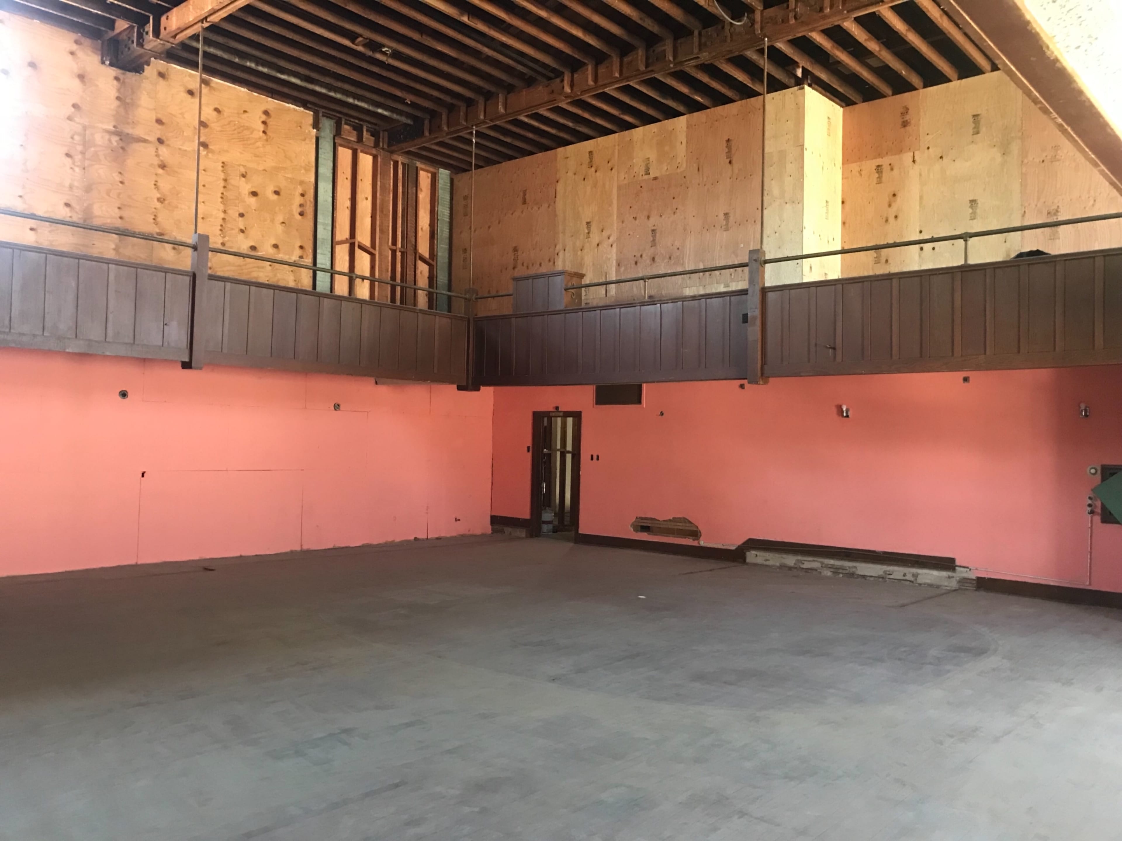 An empty room with pink walls, wooden beams, and a plywood-covered upper level.