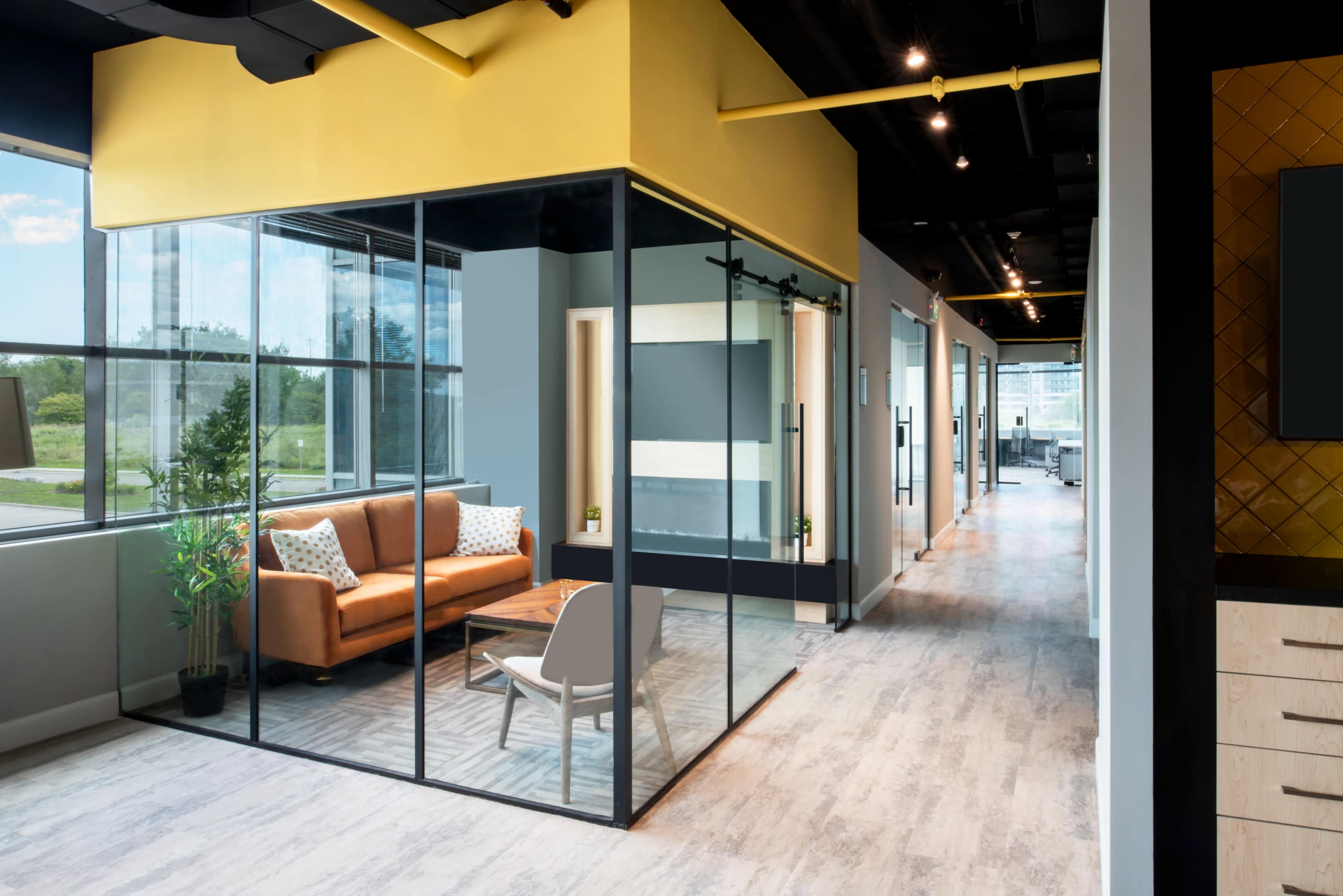 A modern office interior featuring a glass-enclosed meeting room with a brown sofa and a wooden table, flanked by a corridor lined with office doors.