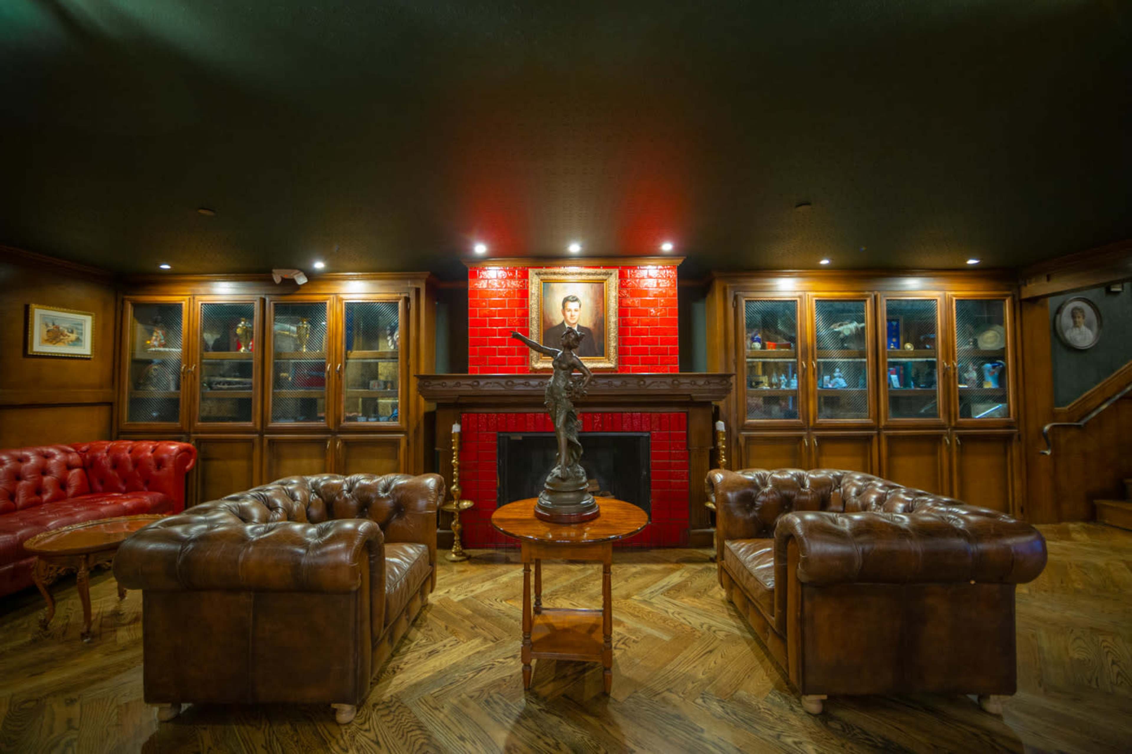 The image shows a room featuring two leather sofas facing each other, a fireplace with a red tiled background, and display cabinets filled with various artifacts and portraits.