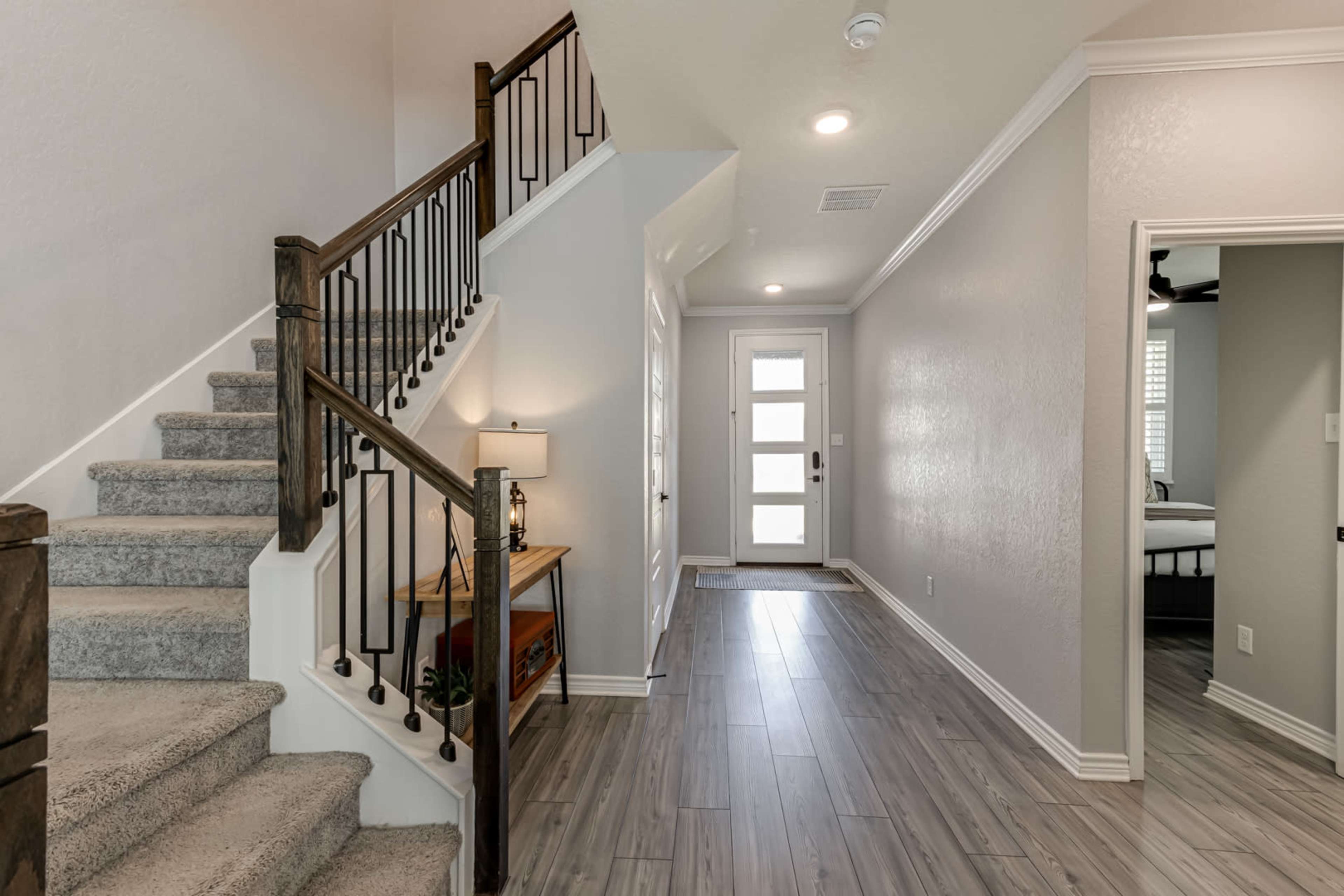 A well-lit entryway featuring a staircase on the left, a console table with a lamp, and a front door directly ahead.
