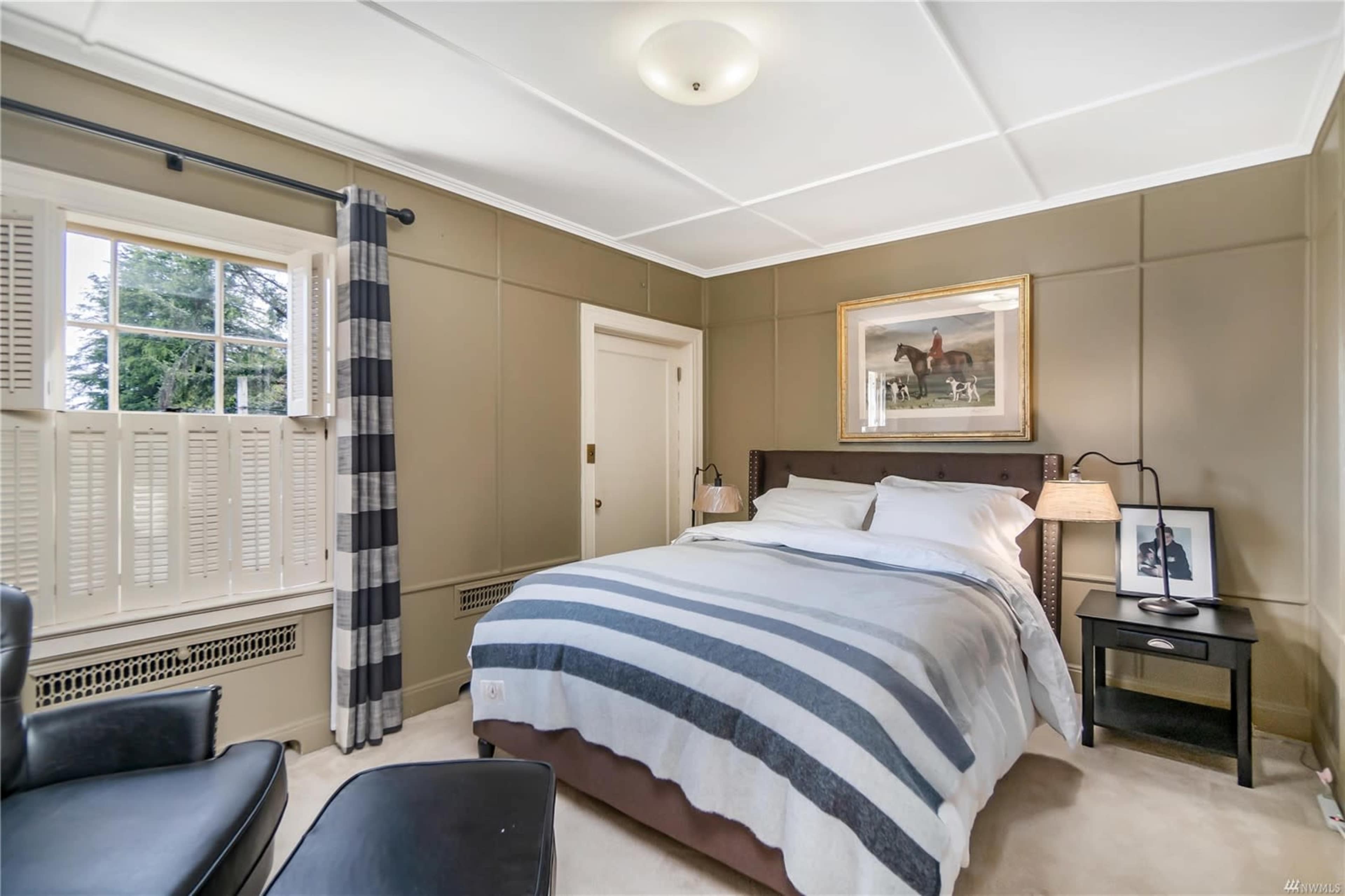 The image shows a neatly arranged bedroom featuring a bed with striped bedding, a black leather chair, and a framed picture on the wall.