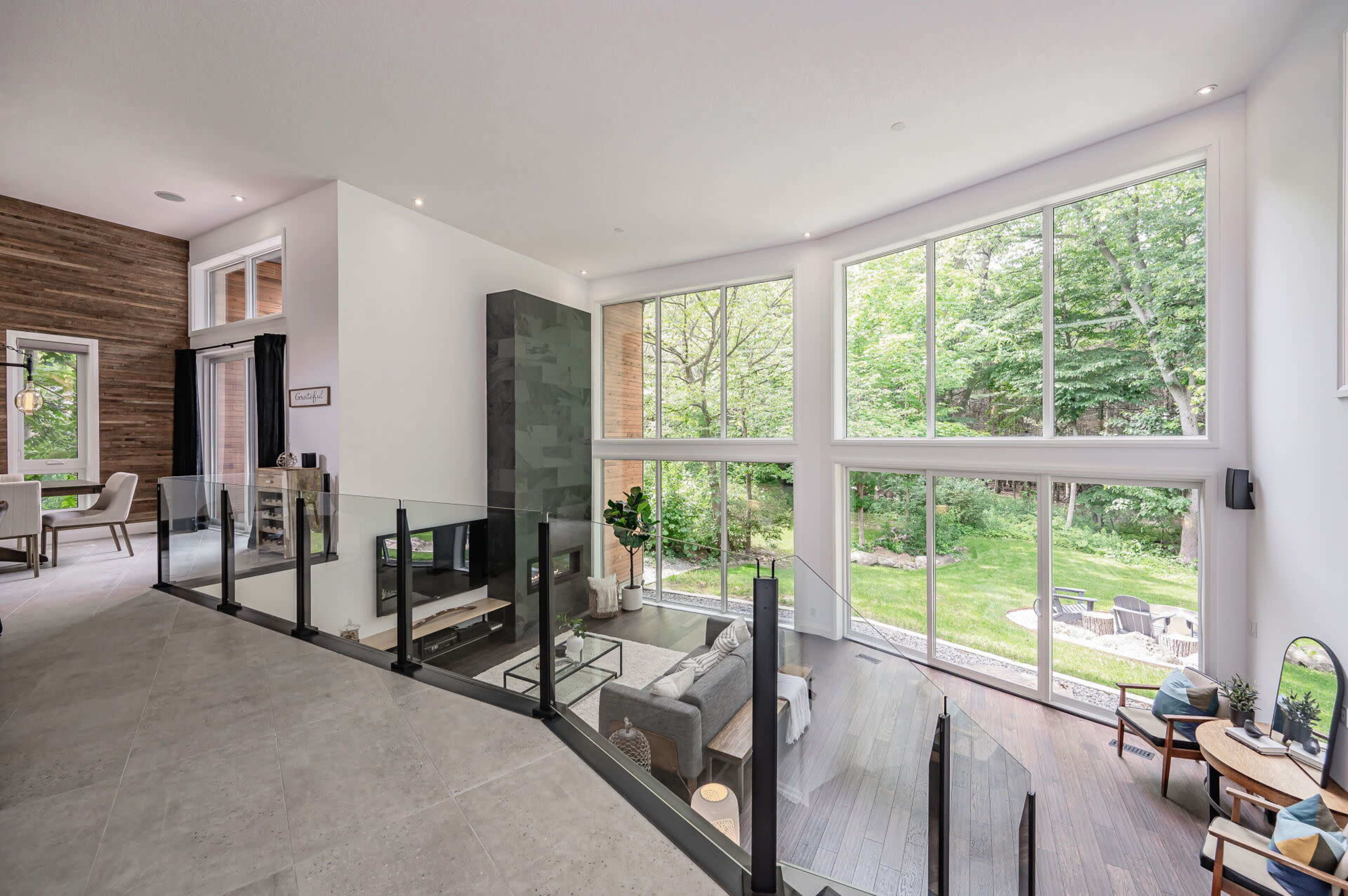 A modern living space features large windows overlooking a forested area, with a mix of wood and stone elements in the design.