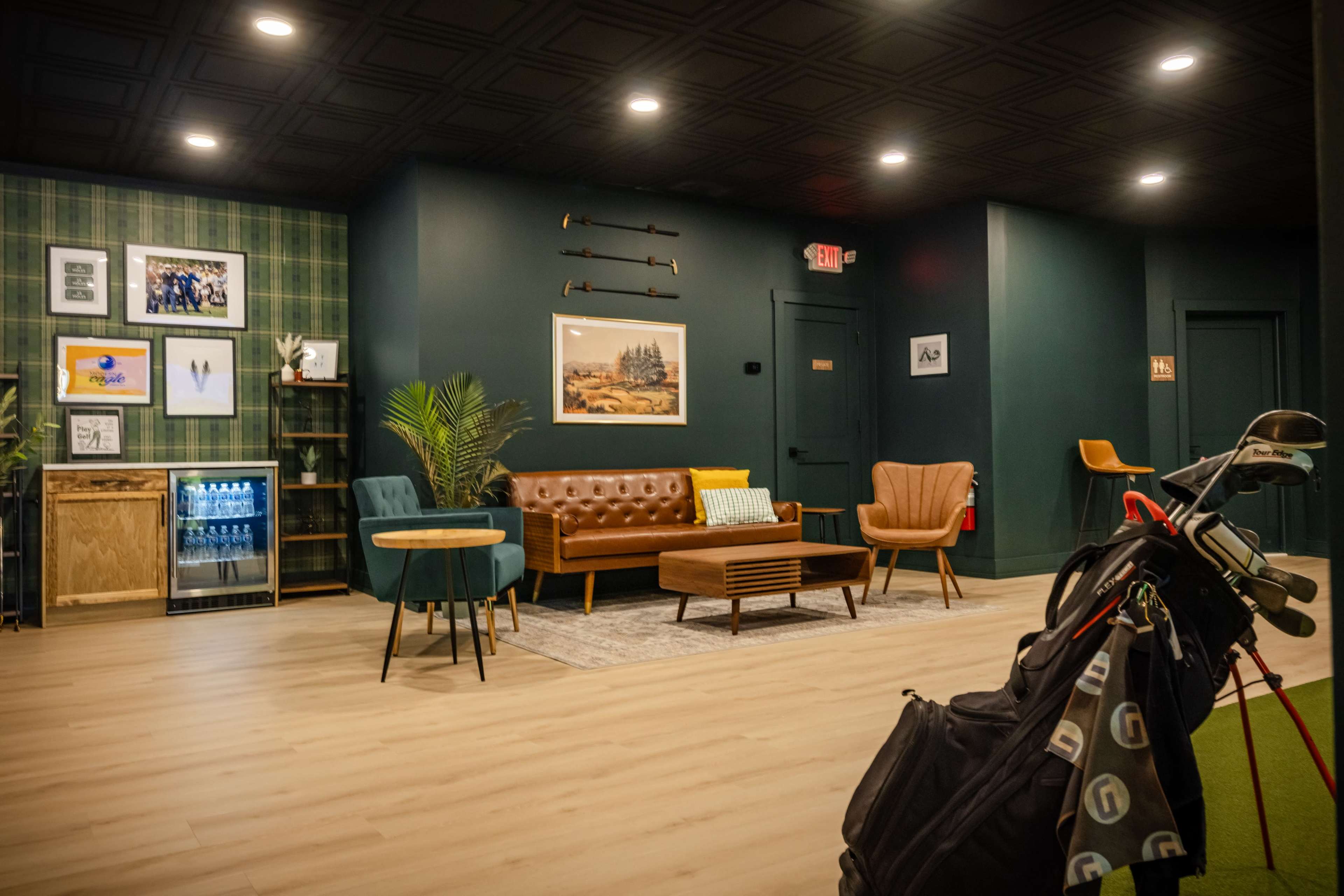 The scene features a modern lounge area with a mix of seating options, including a leather sofa, armchairs, and a coffee table, alongside a golf bag leaning against the wall.
