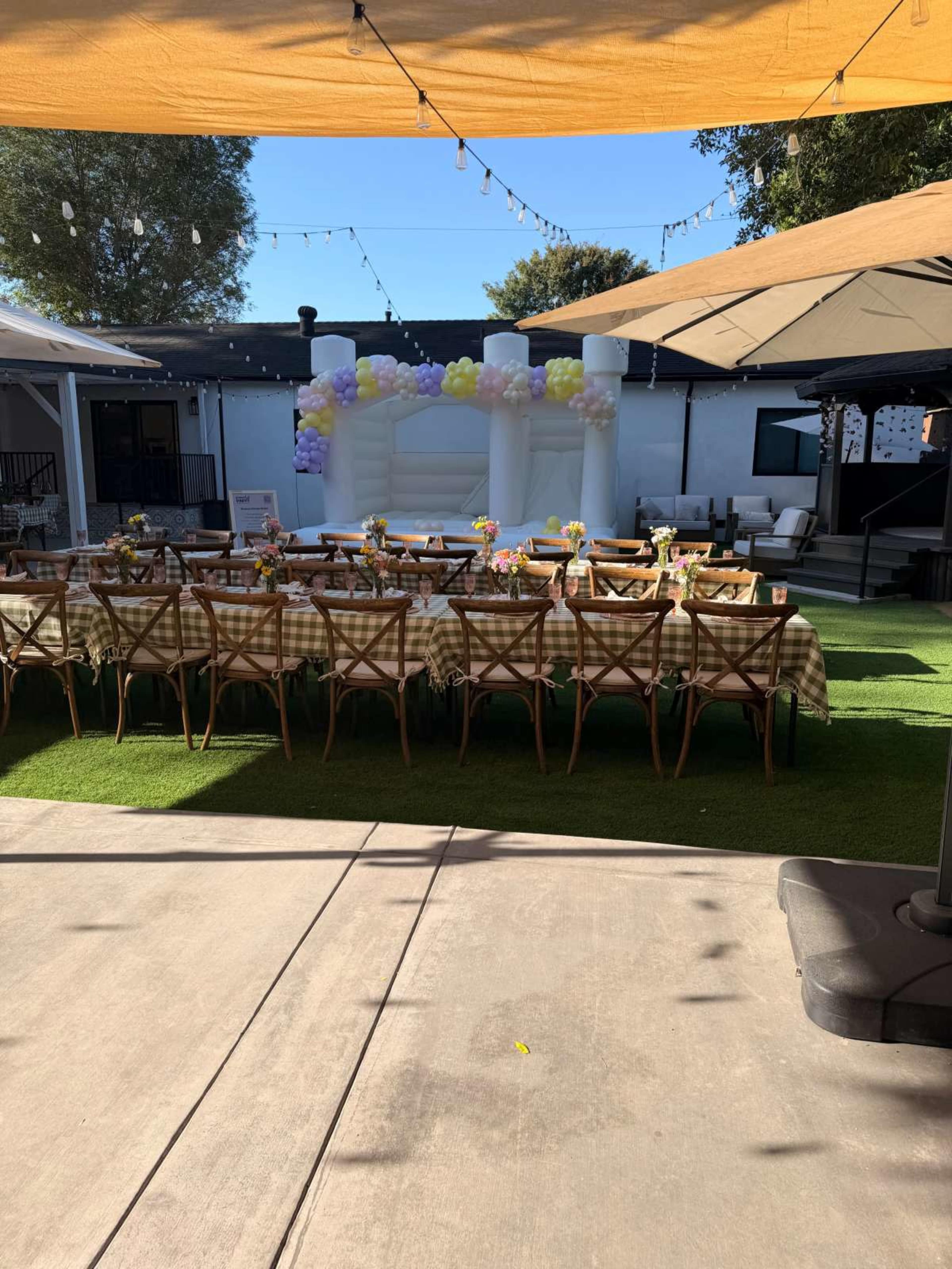 A long banquet table is set up outside under an orange canopy, with colorful balloons and decorations in the background.