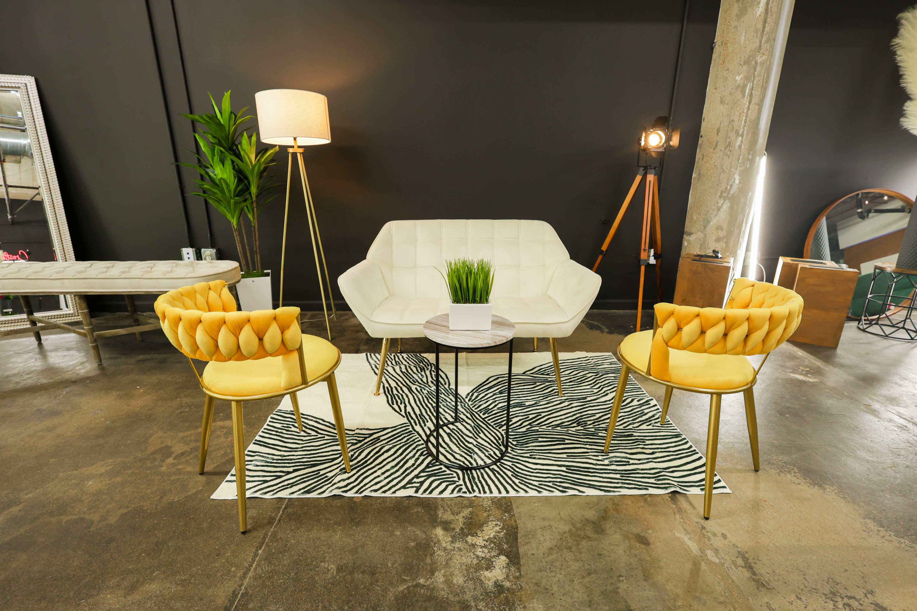 A modern seating area with a light-colored sofa, two yellow chairs, a round coffee table, a floor lamp, and a patterned rug on a concrete floor.
