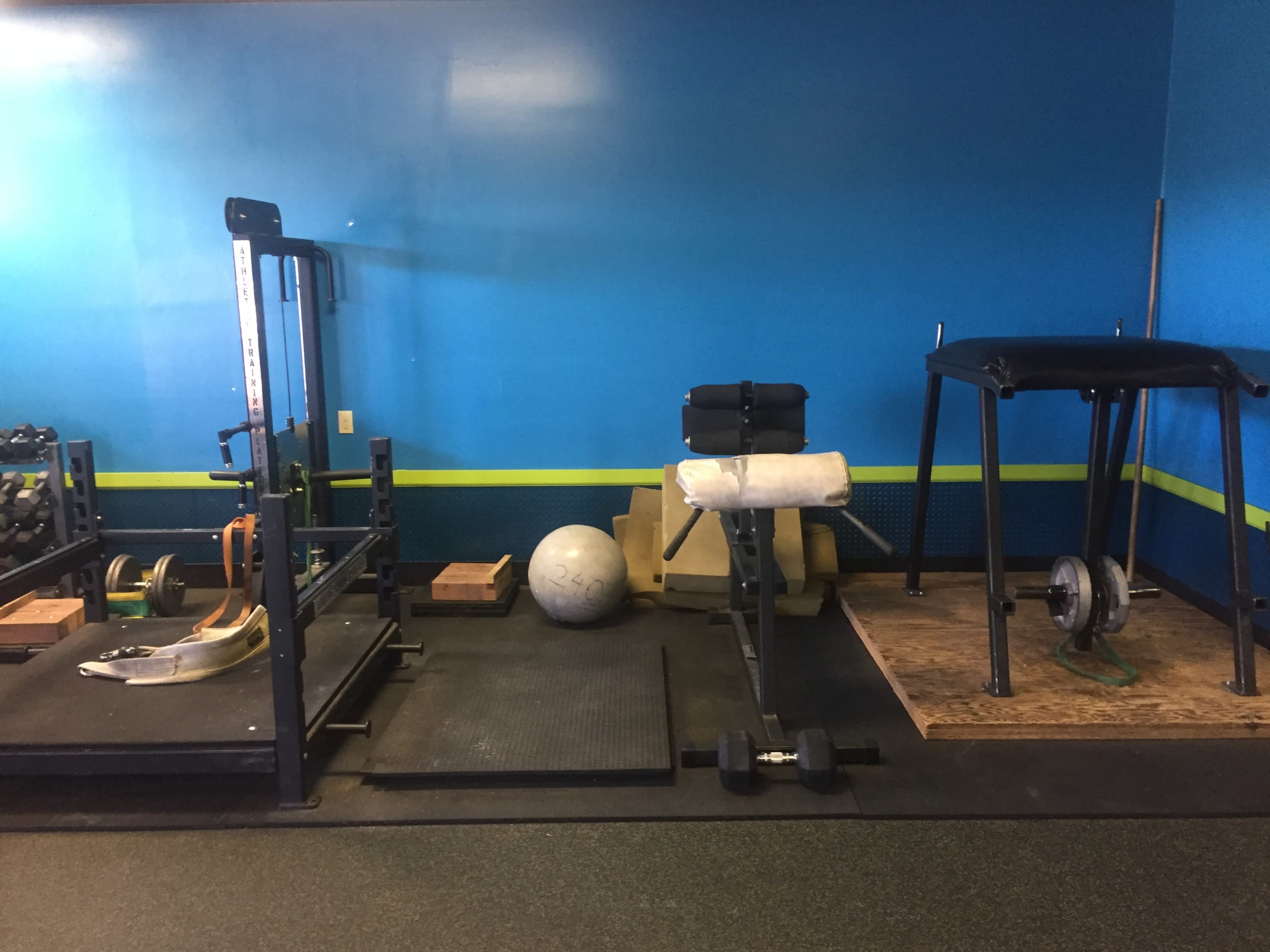 A gym area with weightlifting equipment, including a squat rack, a bench, a stability ball, and a barbell on a weight plate.