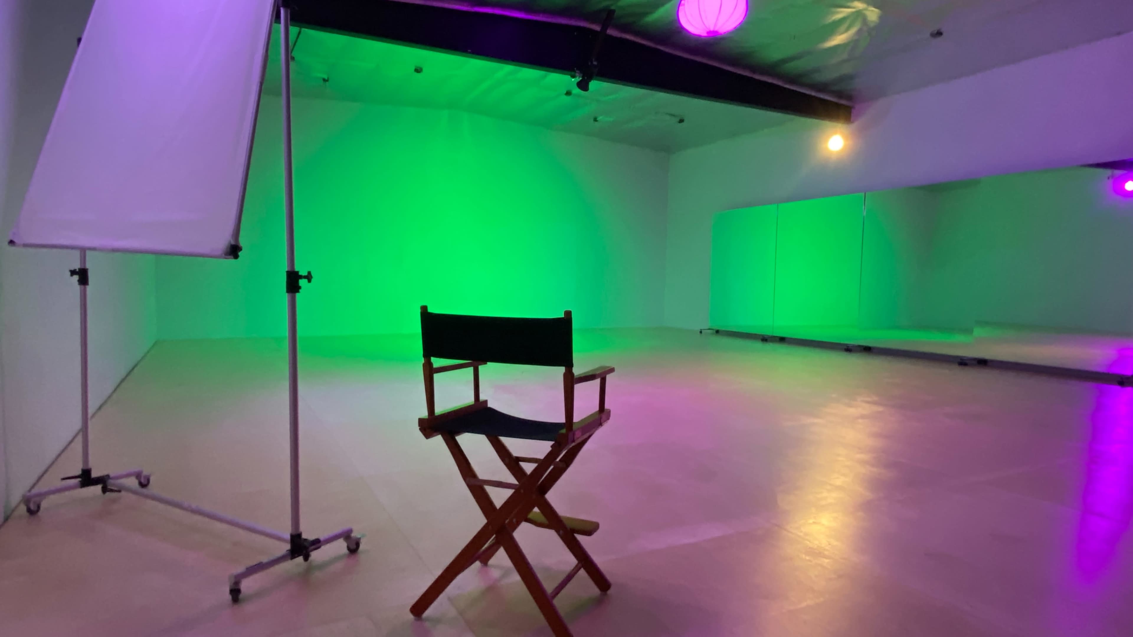 A wooden director's chair is positioned in a green-lit studio with mirrors and minimal furnishings.