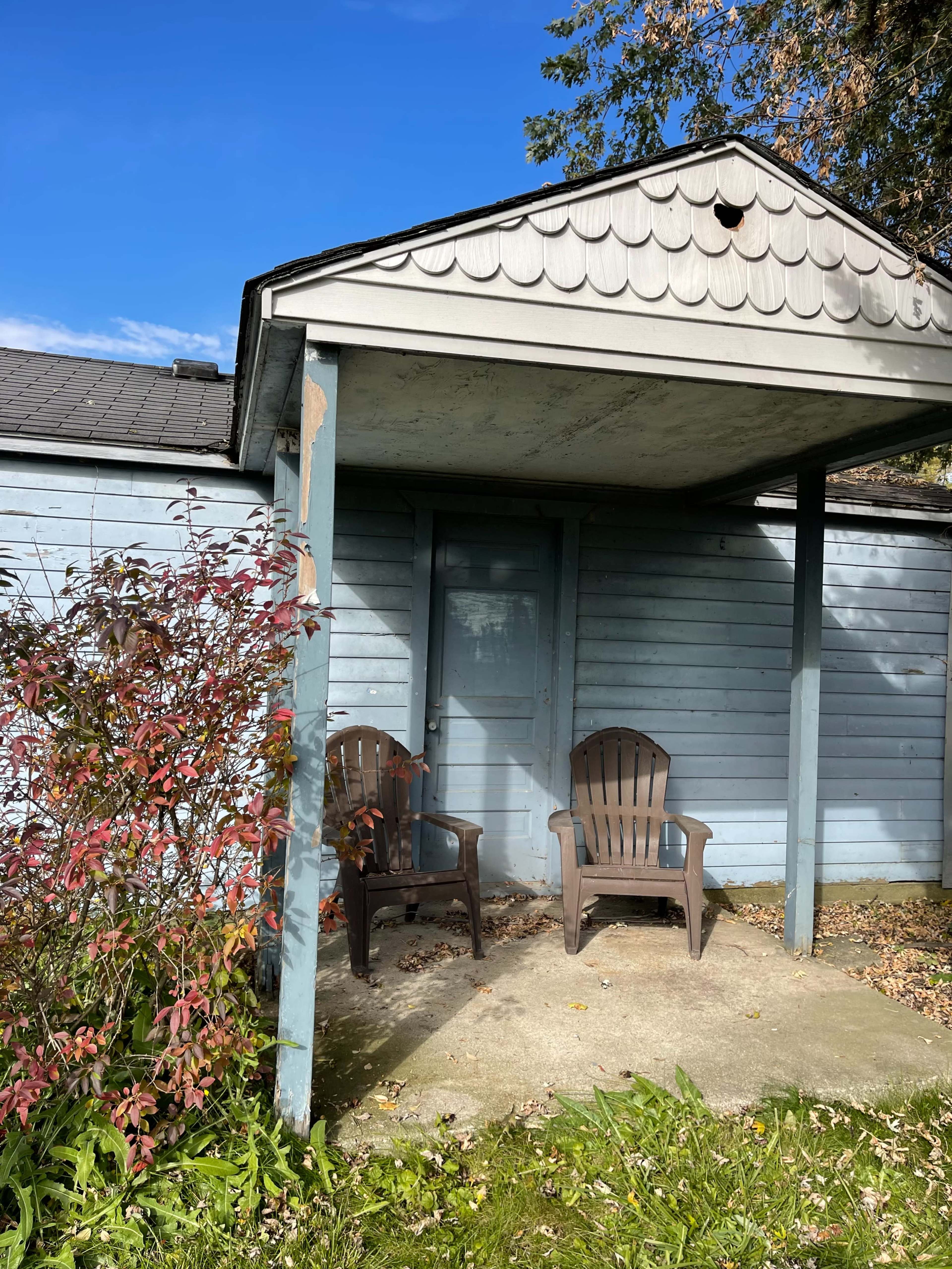 A covered porch with two brown chairs is shown in front of a blue wooden house.