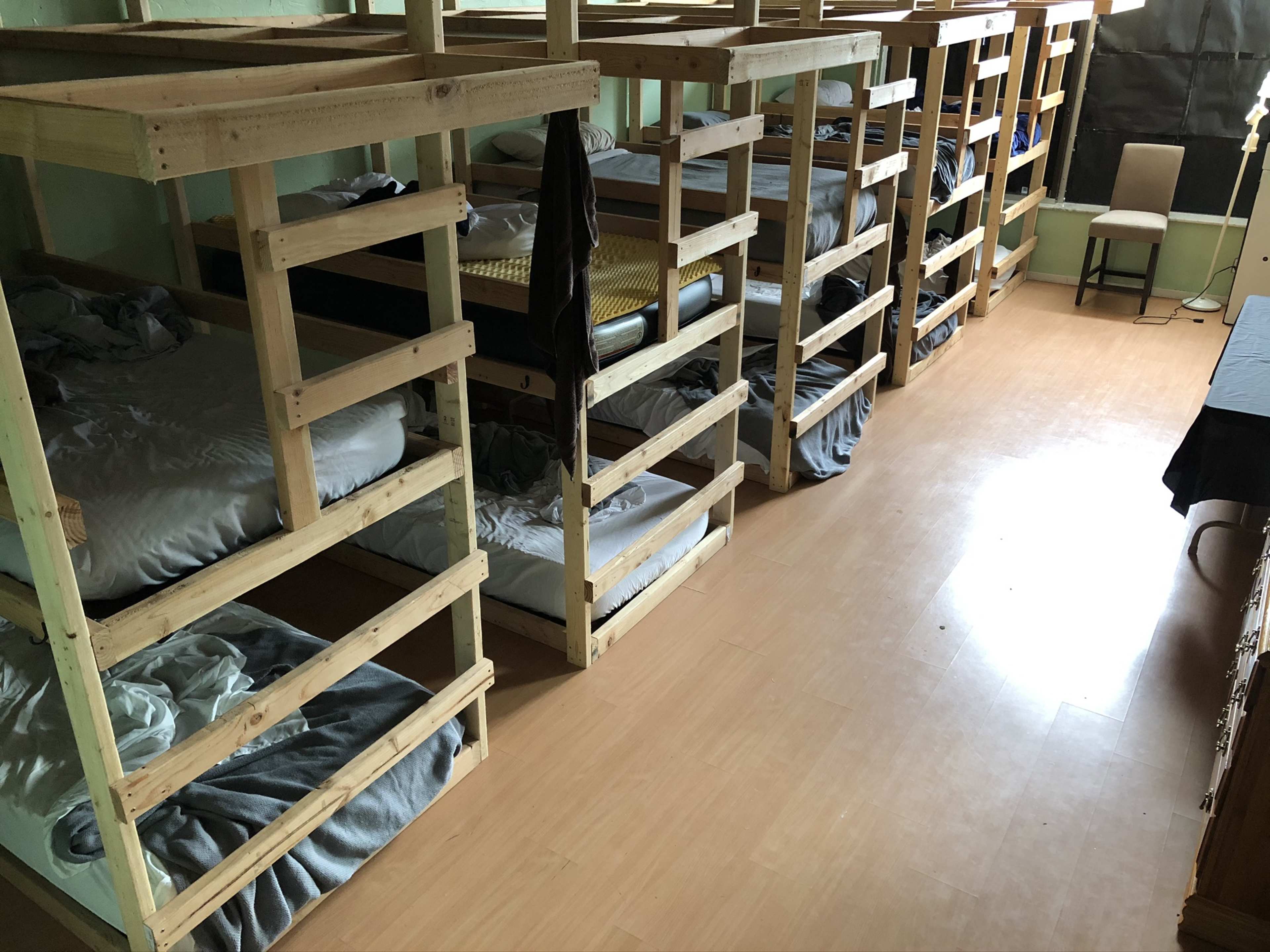A dormitory room with several wooden bunk beds neatly arranged along the walls, each made with unmade bedding.