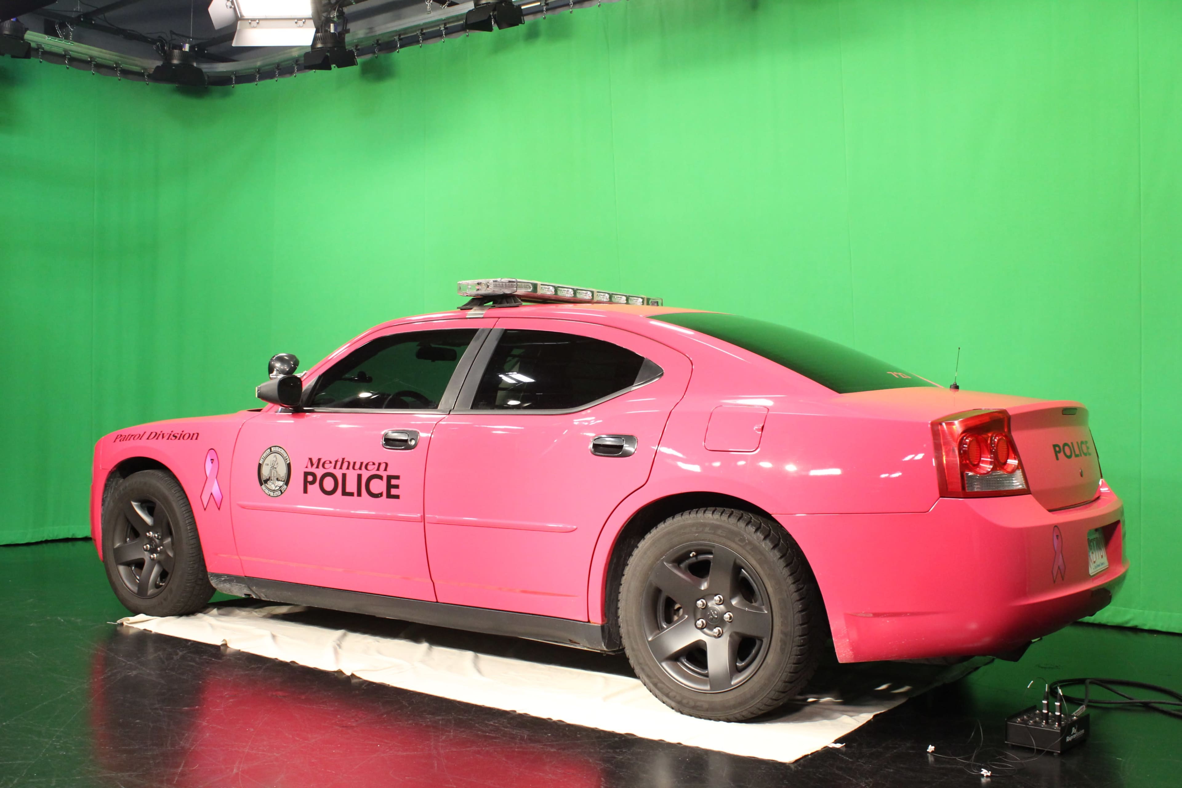 A pink Methuen Police car is parked on a white mat in front of a green screen.