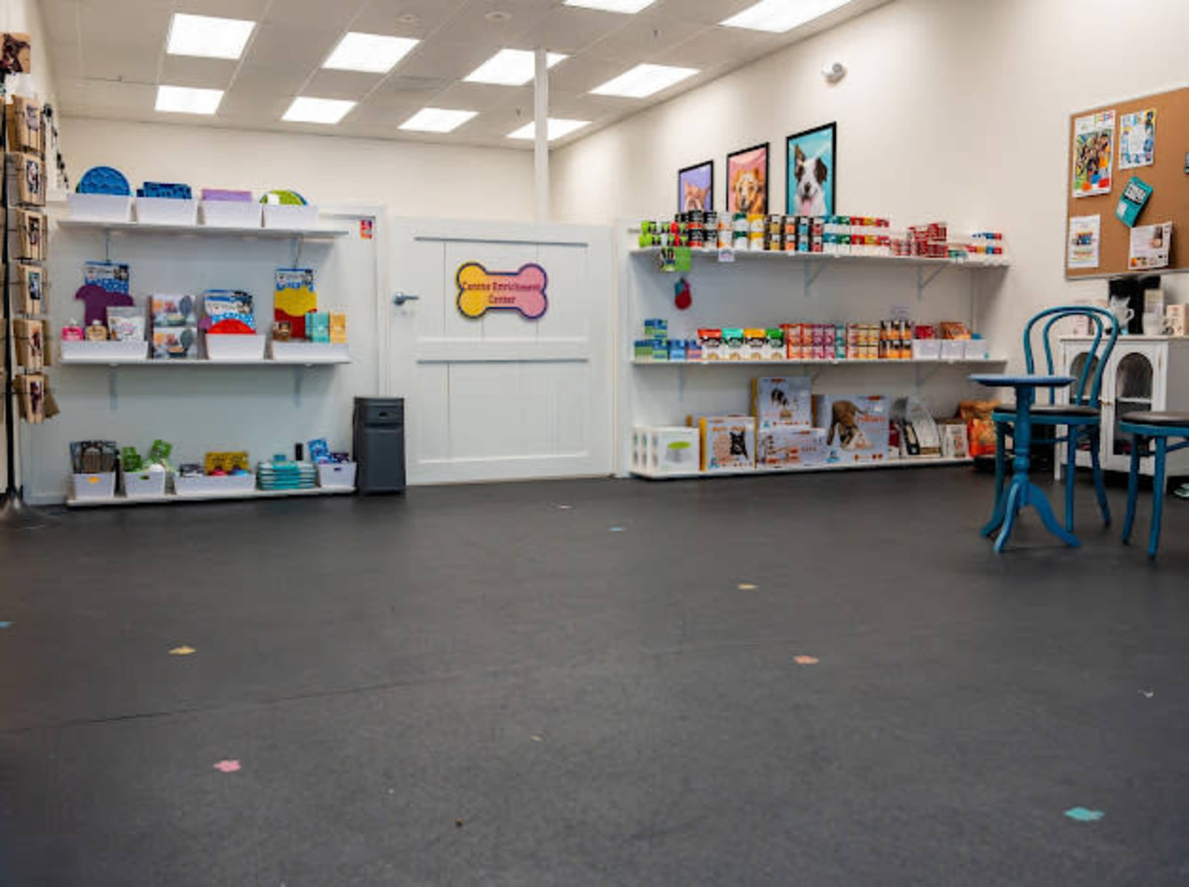 The image shows a well-organized retail space featuring shelves stocked with pet products, including food and toys, along with a blue chair and a bulletin board on the wall.