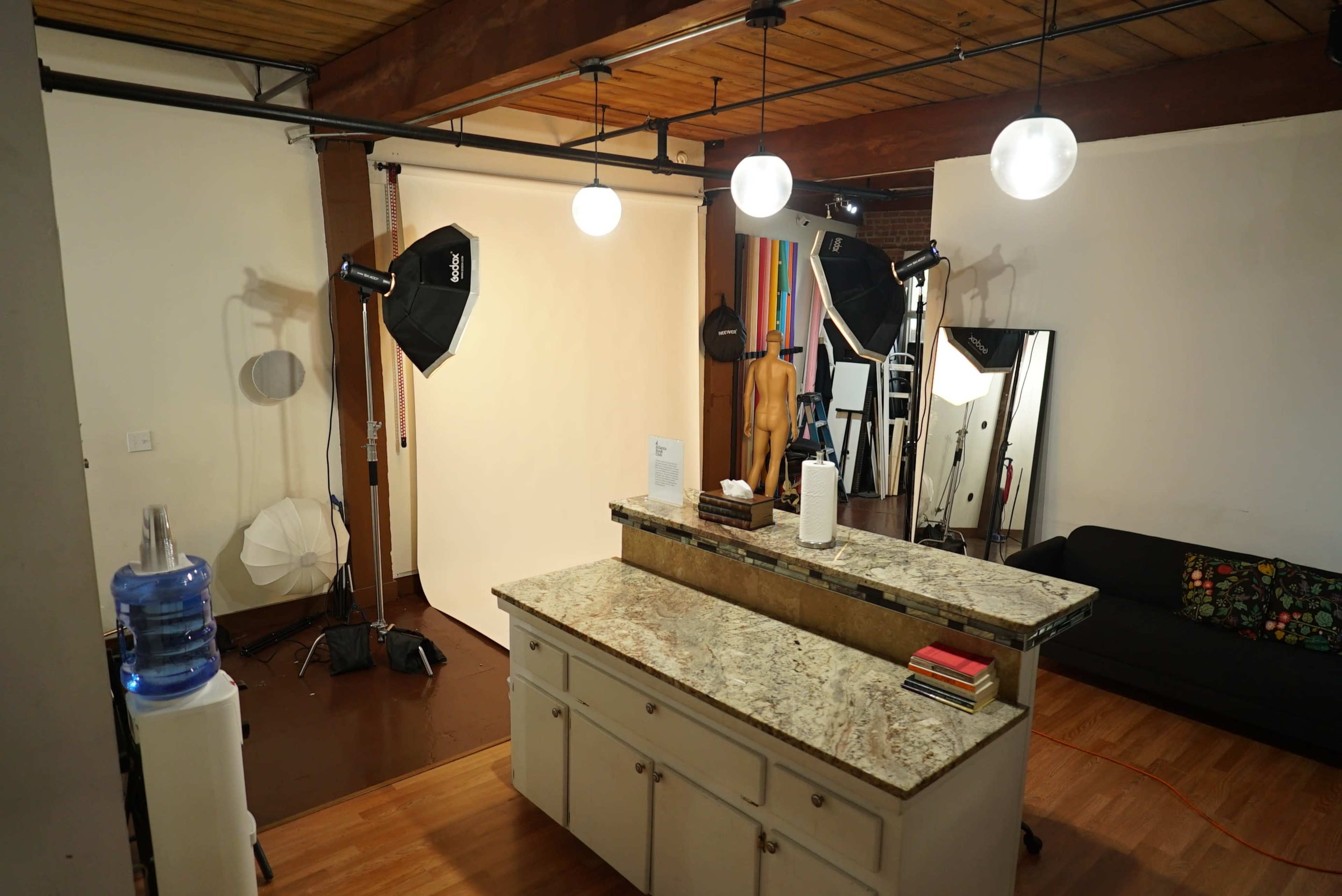 The image shows a photography studio with a granite kitchen island, several lighting setups, a blank backdrop, and a large mirror against the wall.