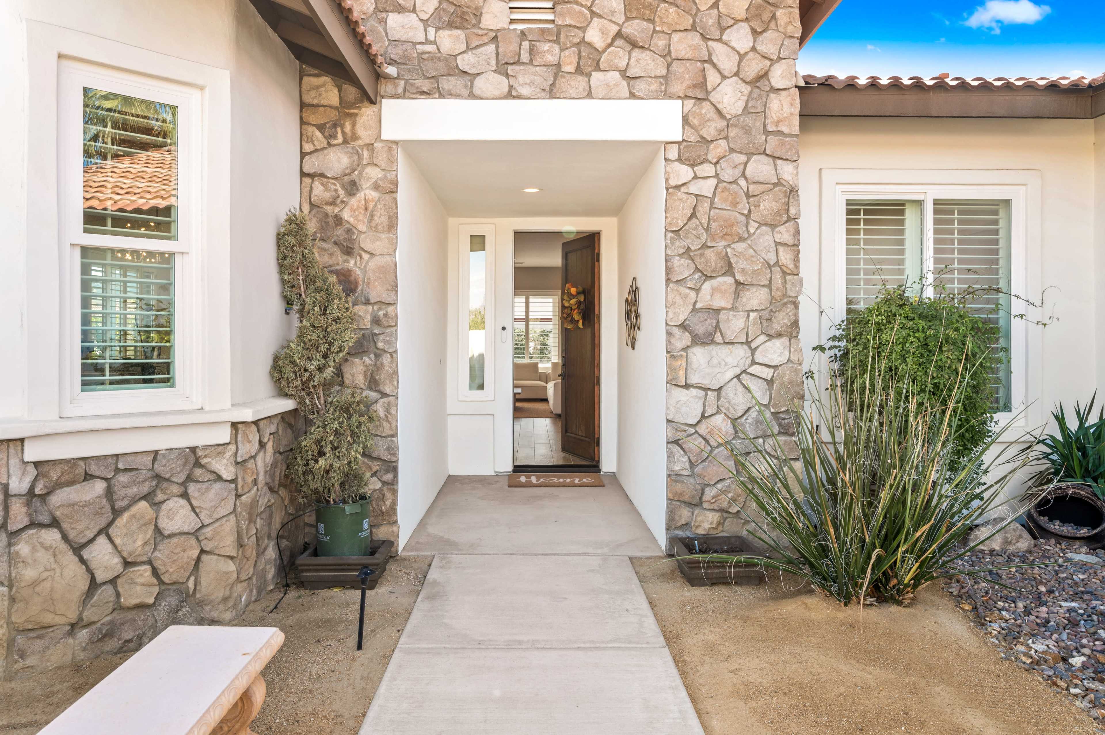The entrance features a stone facade flanked by landscaped areas and a clear walkway leading to the front door.