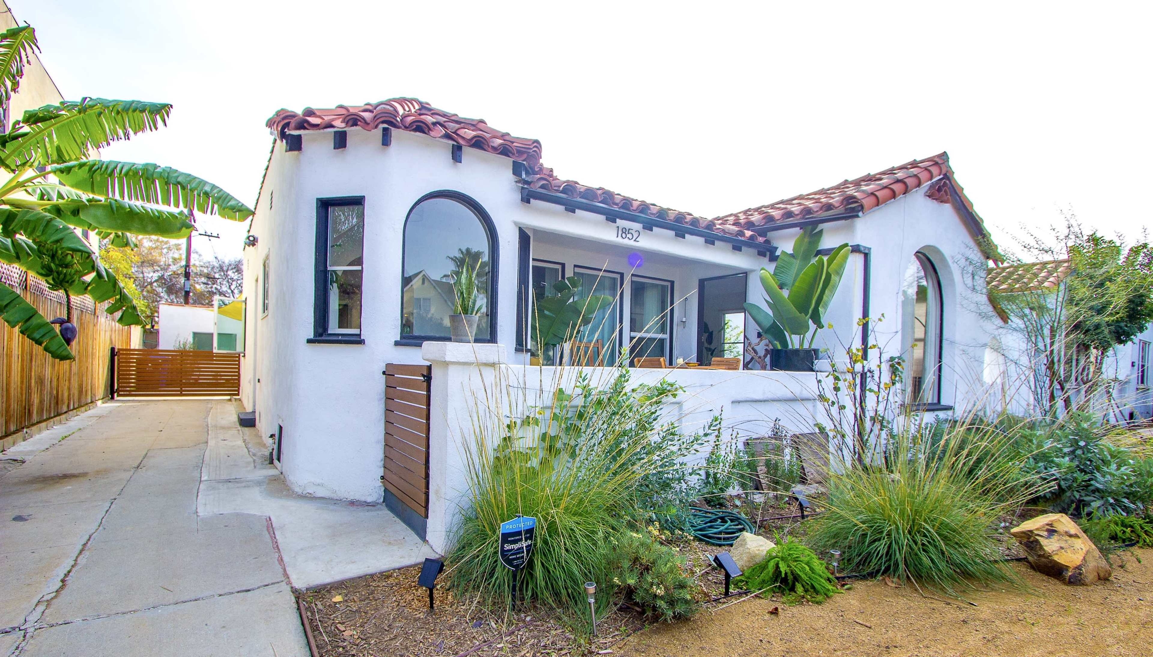 A single-family home with a tiled roof and arched windows surrounded by tropical plants and a gravel landscape.