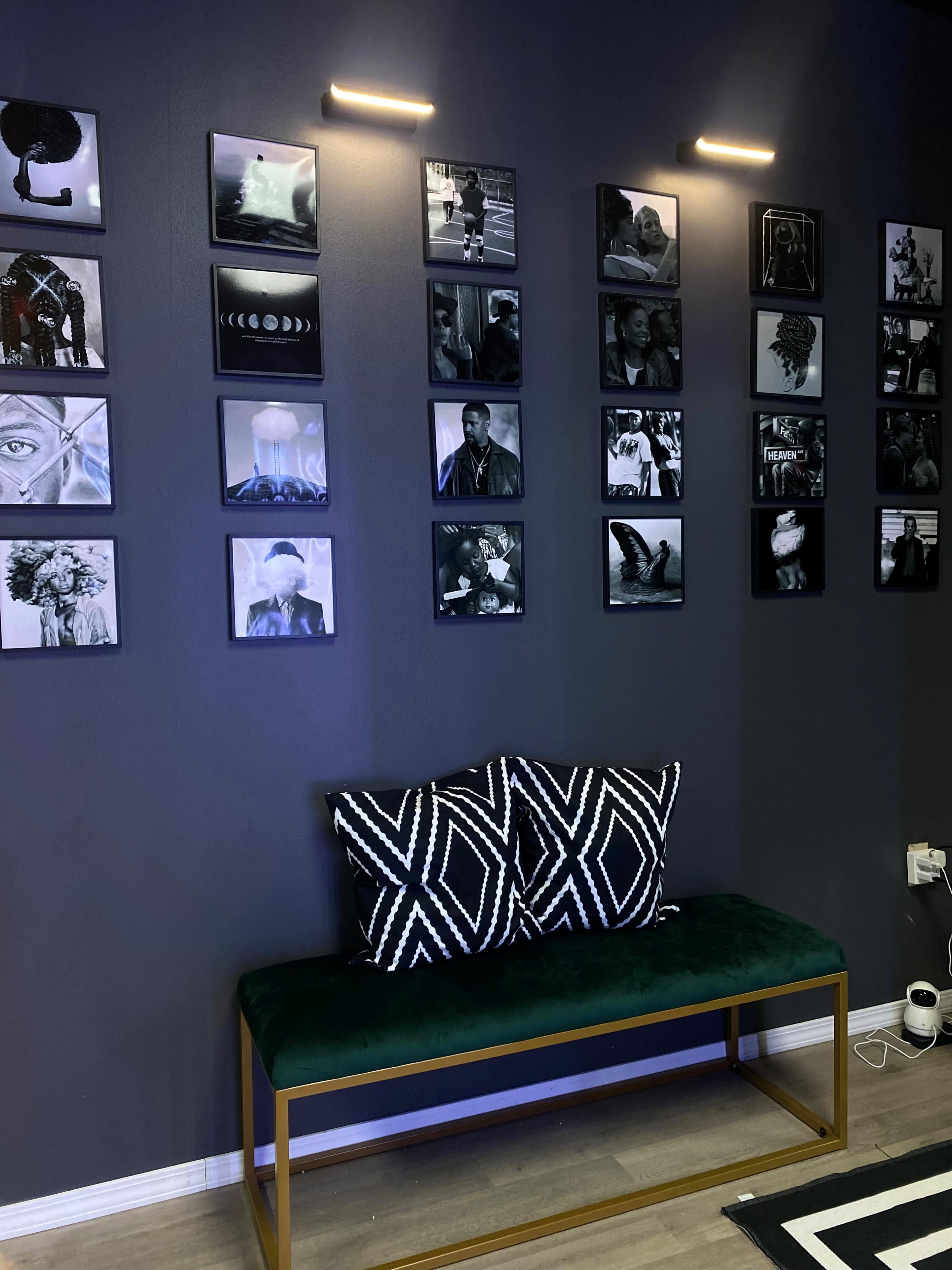 A dark wall adorned with black and white photographs arranged in a grid above a green bench with patterned cushions.