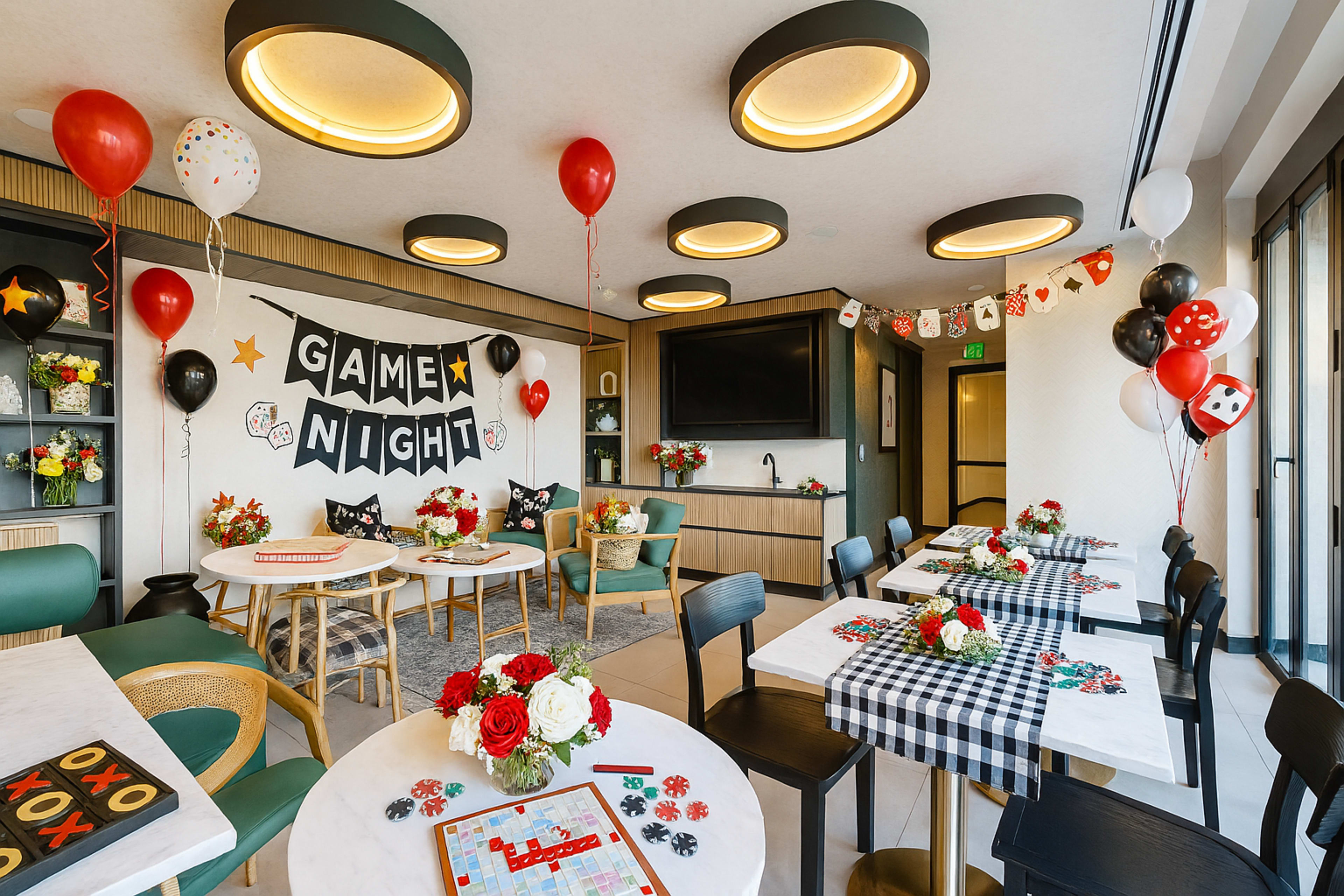 The image shows a cozy game night setup with decorated tables, party balloons, and cheerful signage in a well-lit room.